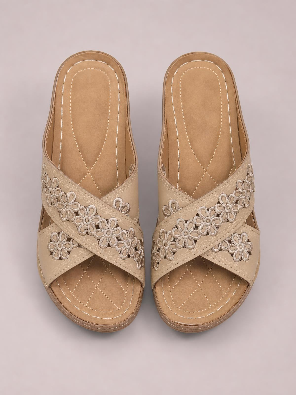 Tan crisscross flower wedge sandals feature open toes, floral appliqué straps, stitched footbeds, and low wedge soles for comfortable everyday wear.