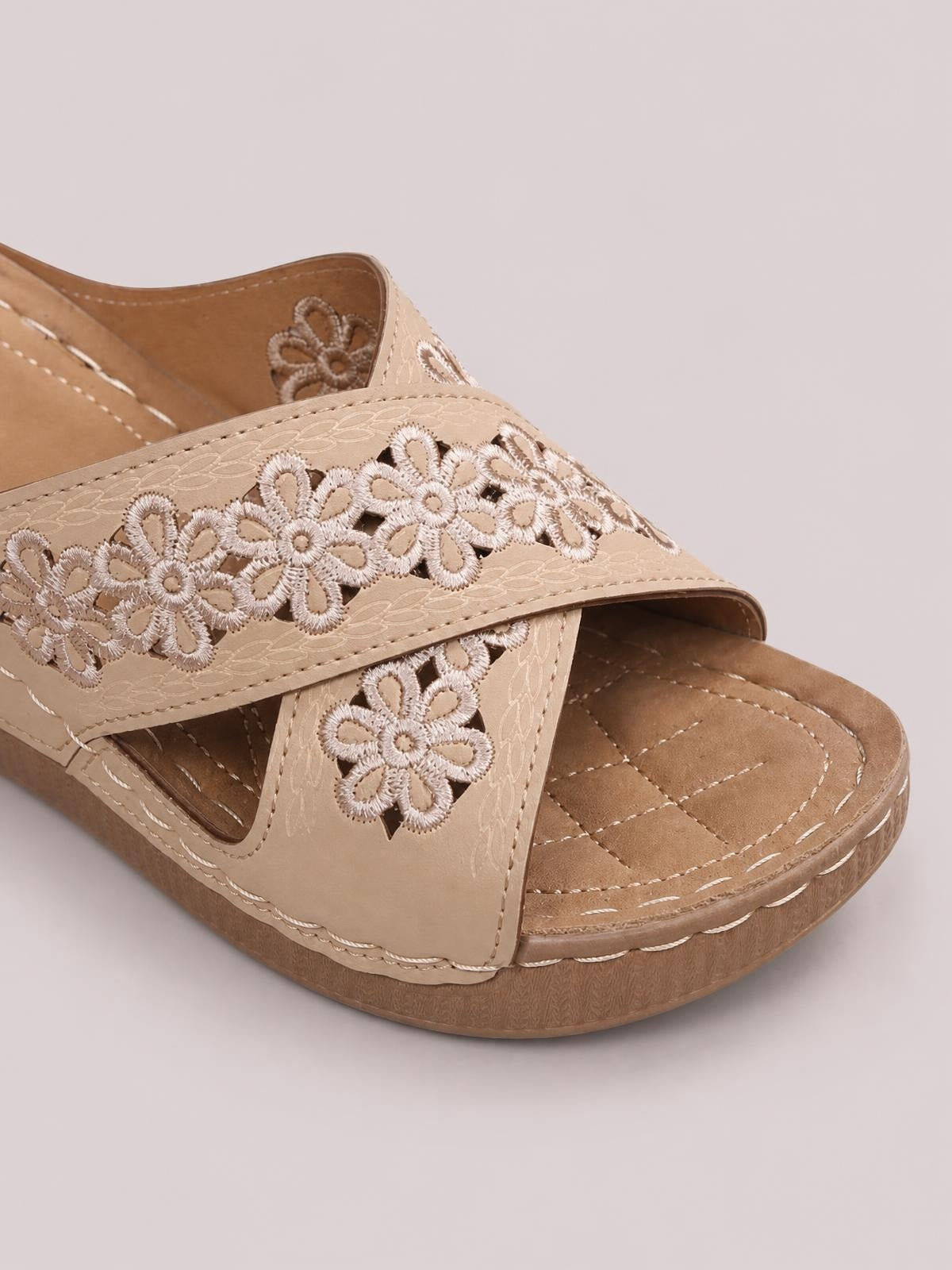 Close-up of beige crisscross flower wedge sandals with embroidered floral straps, stitched PU leather construction, cushioned footbeds, and low platform heels.