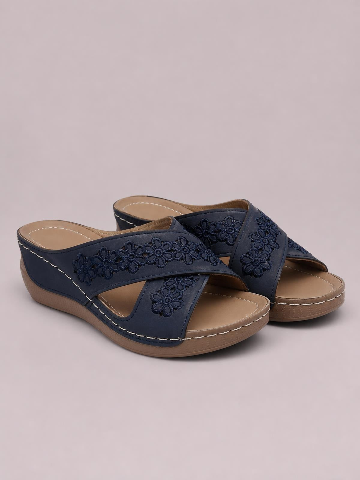 Navy crisscross flower wedge sandals feature open toes, floral detailing, low wedge heels, tan footbeds, and contrasting stitched trim.