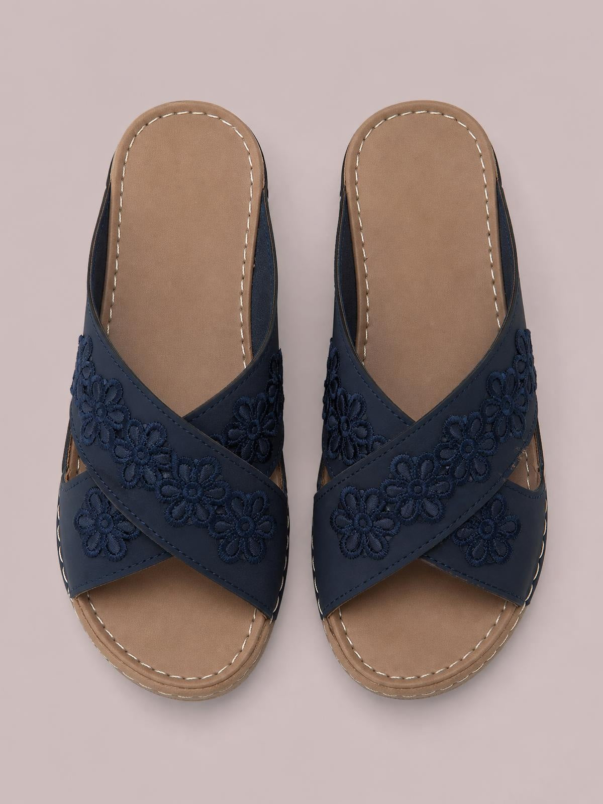 Navy crisscross flower wedge sandals feature embroidered floral straps, open toes, cushioned tan footbeds, and low wedge soles with contrast stitching.