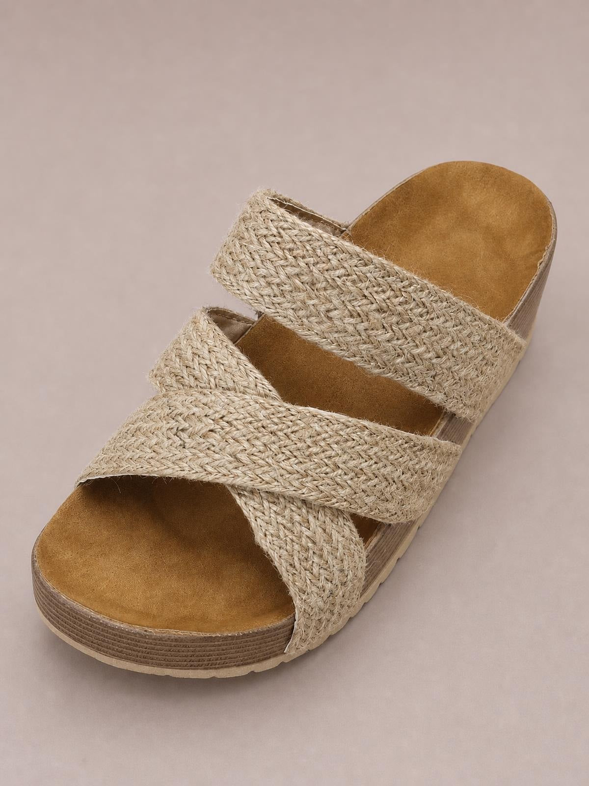 Beige open-toe platform sandals feature wide crisscross woven straps, cushioned footbeds, and textured layered soles with a flat silhouette.