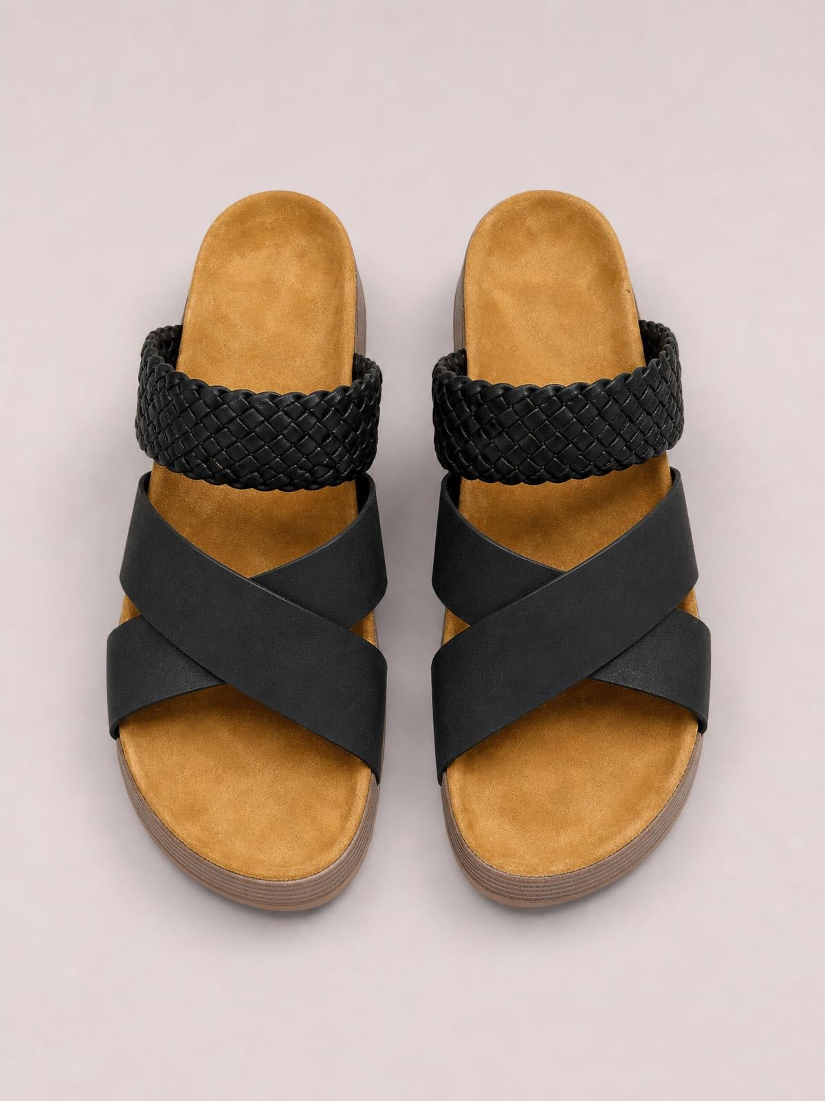 Black crisscross open-toe platform sandals feature wide overlapping straps, a braided upper band, tan footbeds, and flat rubber soles.