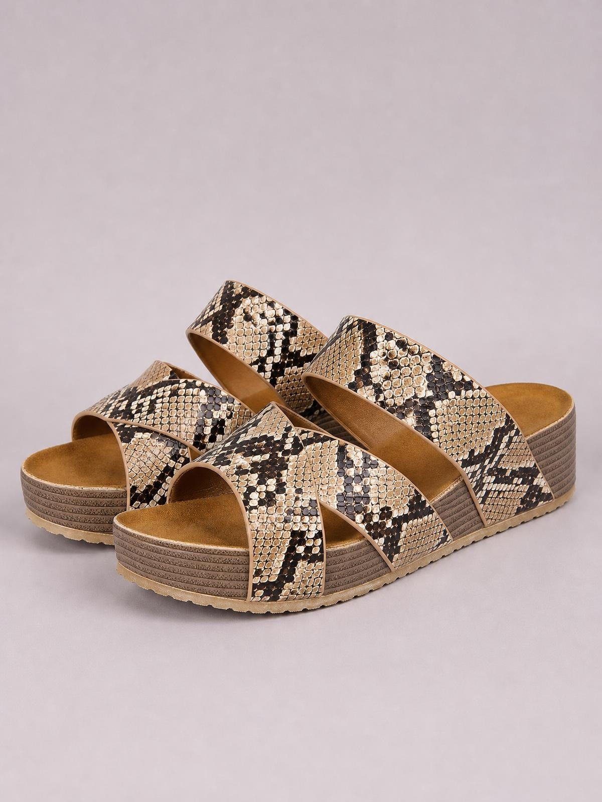 Tan-and-black snakeskin sandals feature crisscross open-toe straps and a thick flat platform sole with textured layered construction.