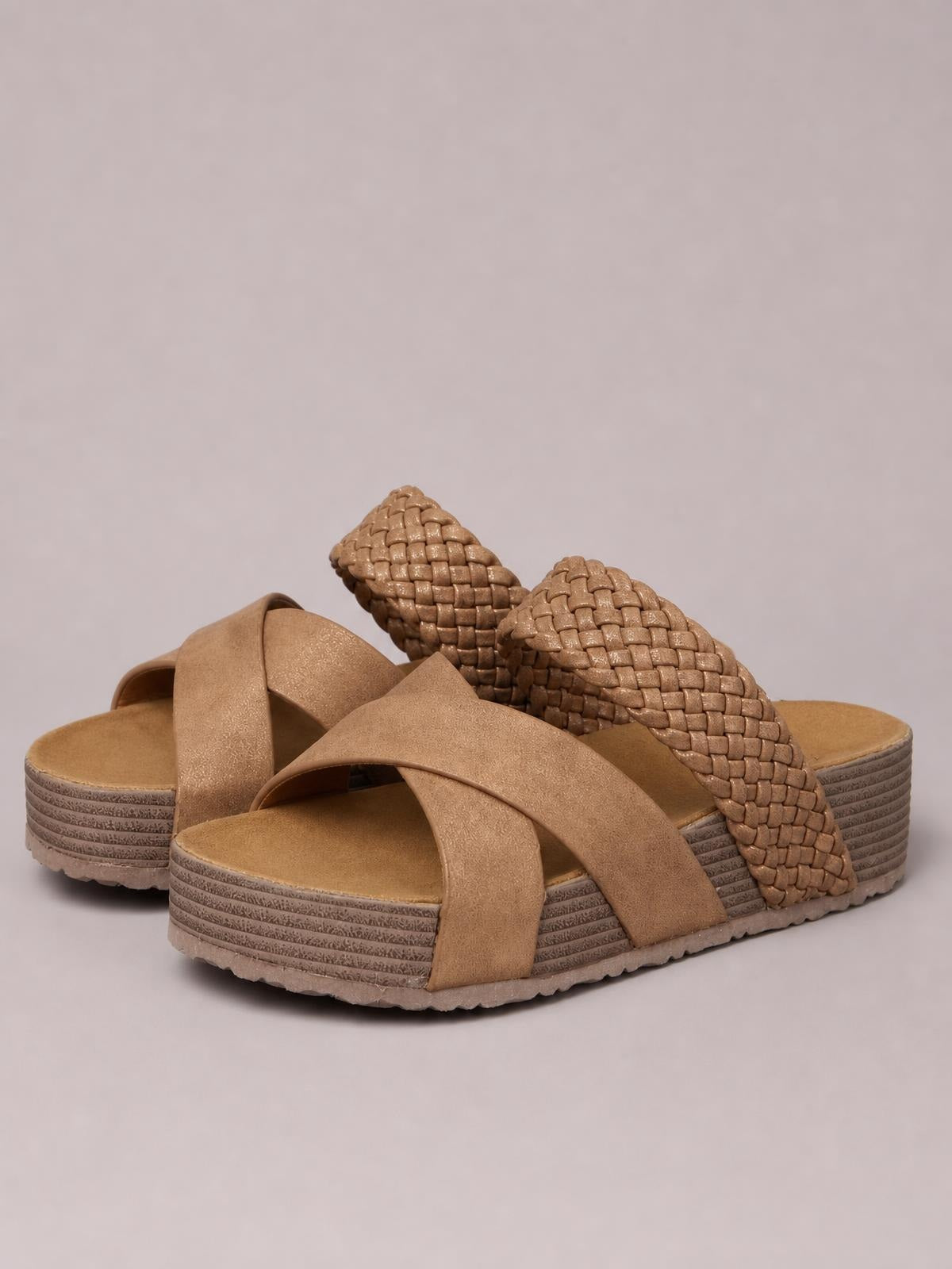 Tan crisscross open-toe platform sandals feature wide overlapping straps, woven textured heel bands, and layered rubber soles with a flat profile.