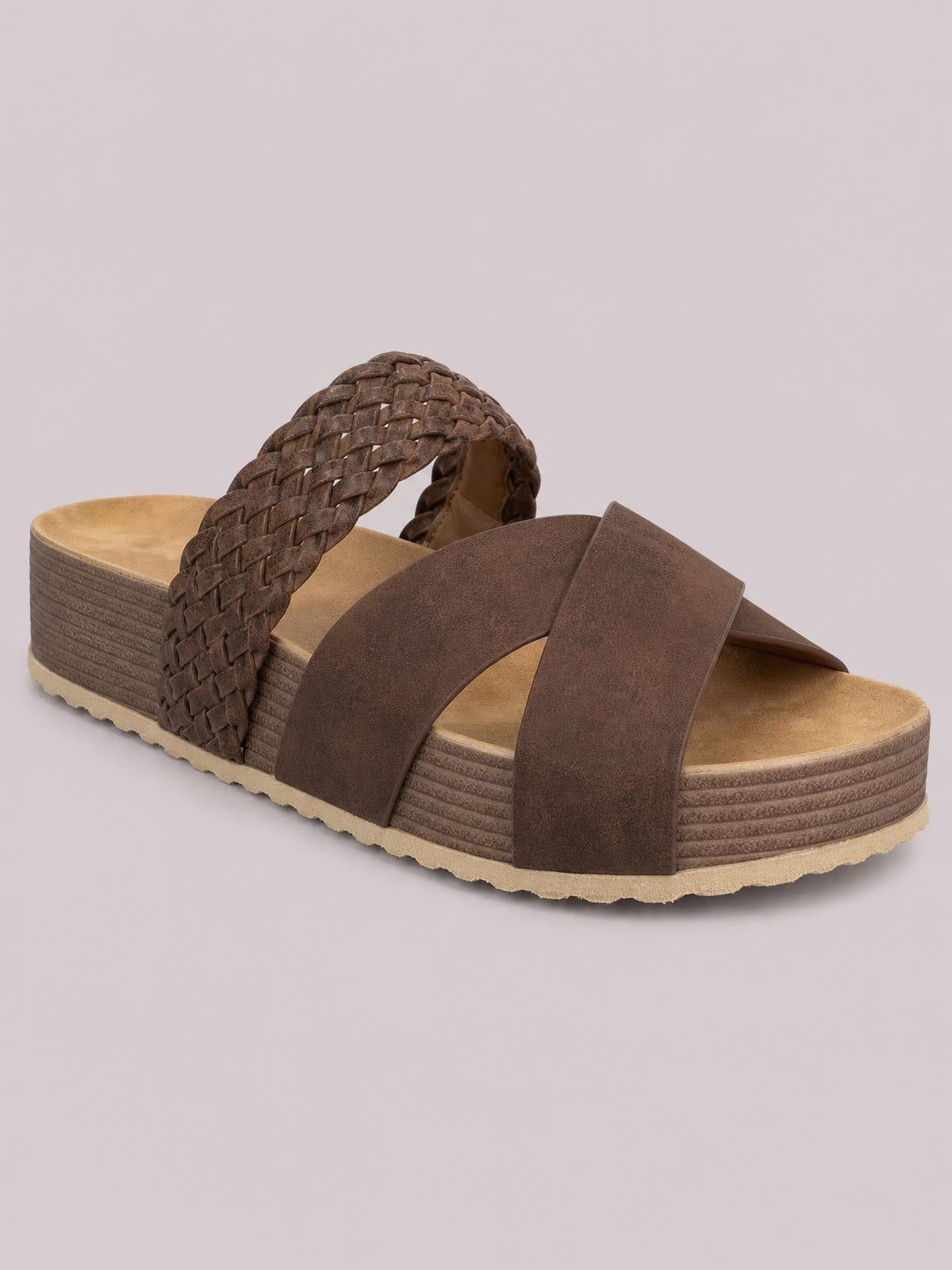Brown open-toe platform sandals feature wide crisscross straps, a braided back strap, and a textured flat wedge sole with layered construction.