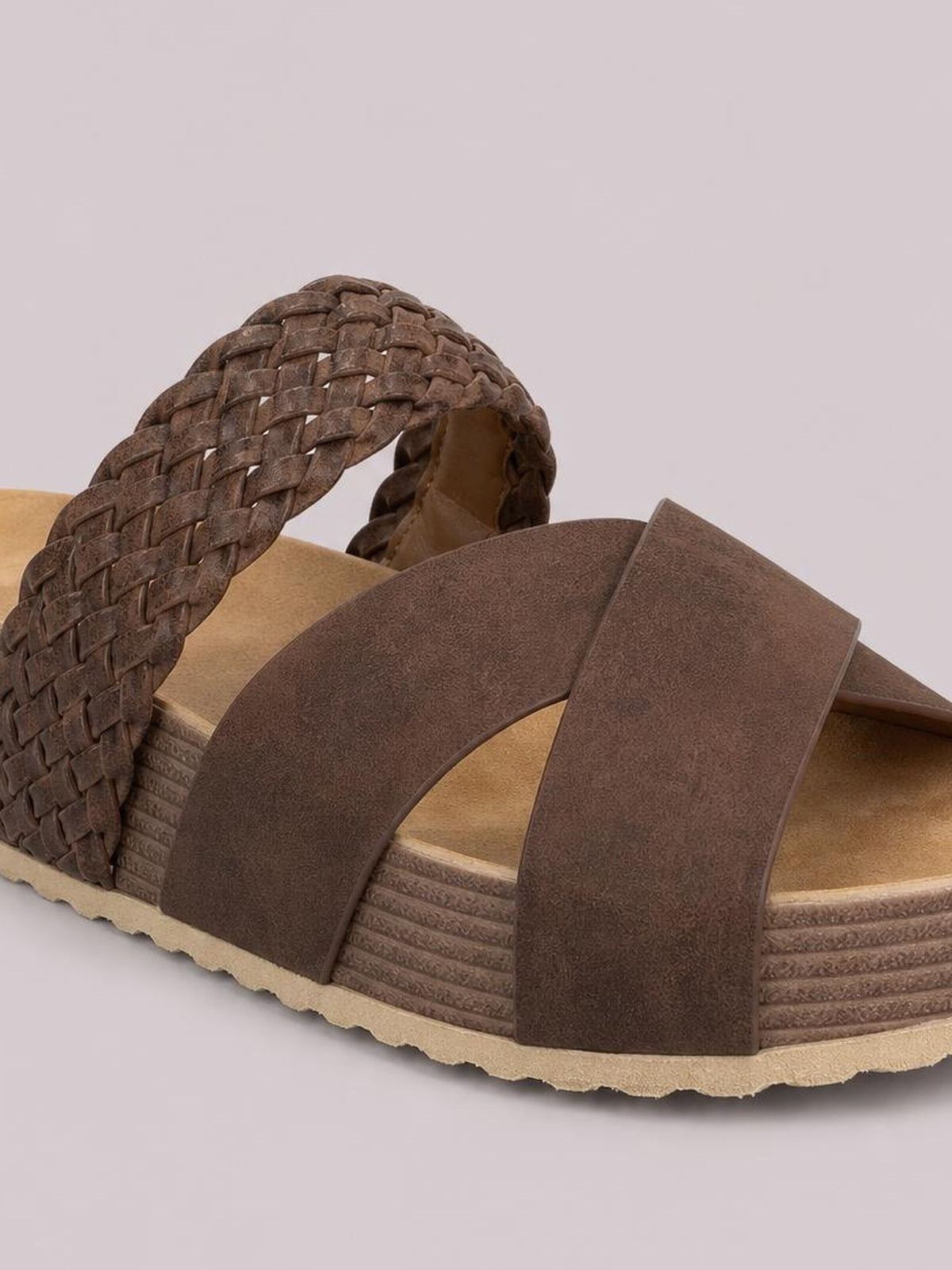 Brown open-toe platform sandal featuring wide crisscross straps, a braided back strap, textured layered sole, and flat platform construction.