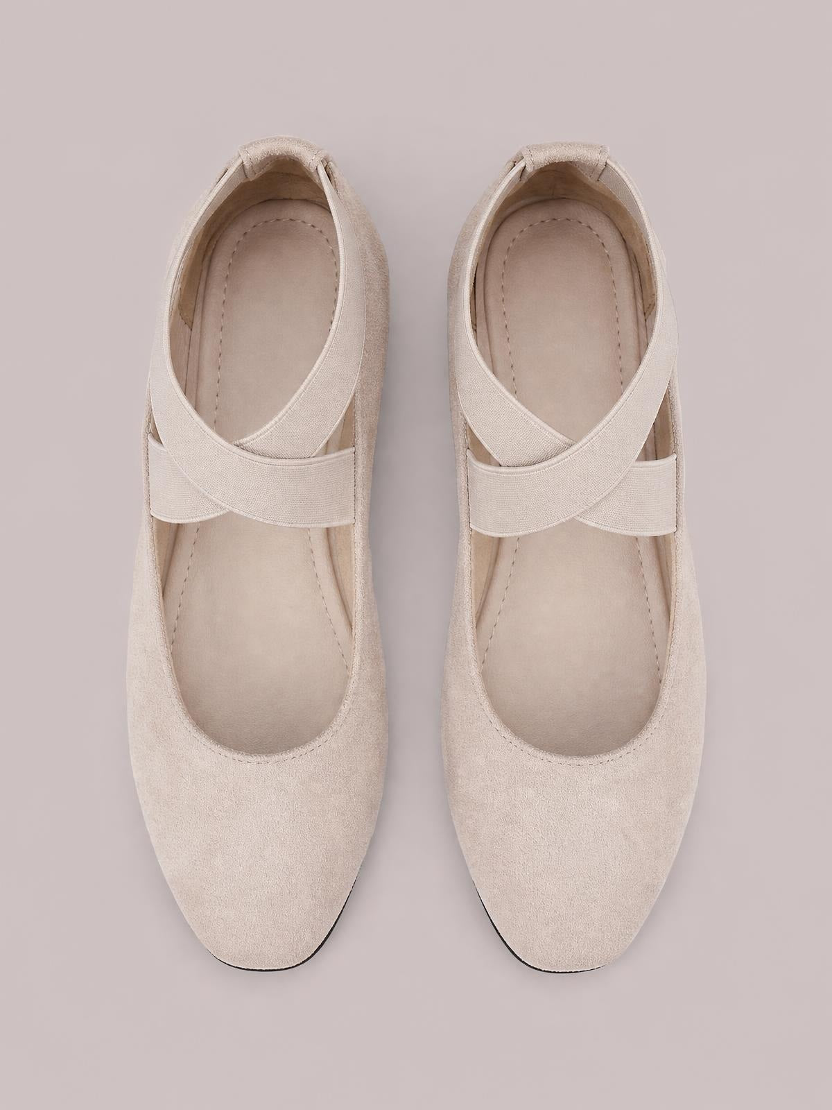 Beige suede point-toe flat slip-ons with crisscross straps, rounded silhouettes, stitched insoles, and low rubber soles.