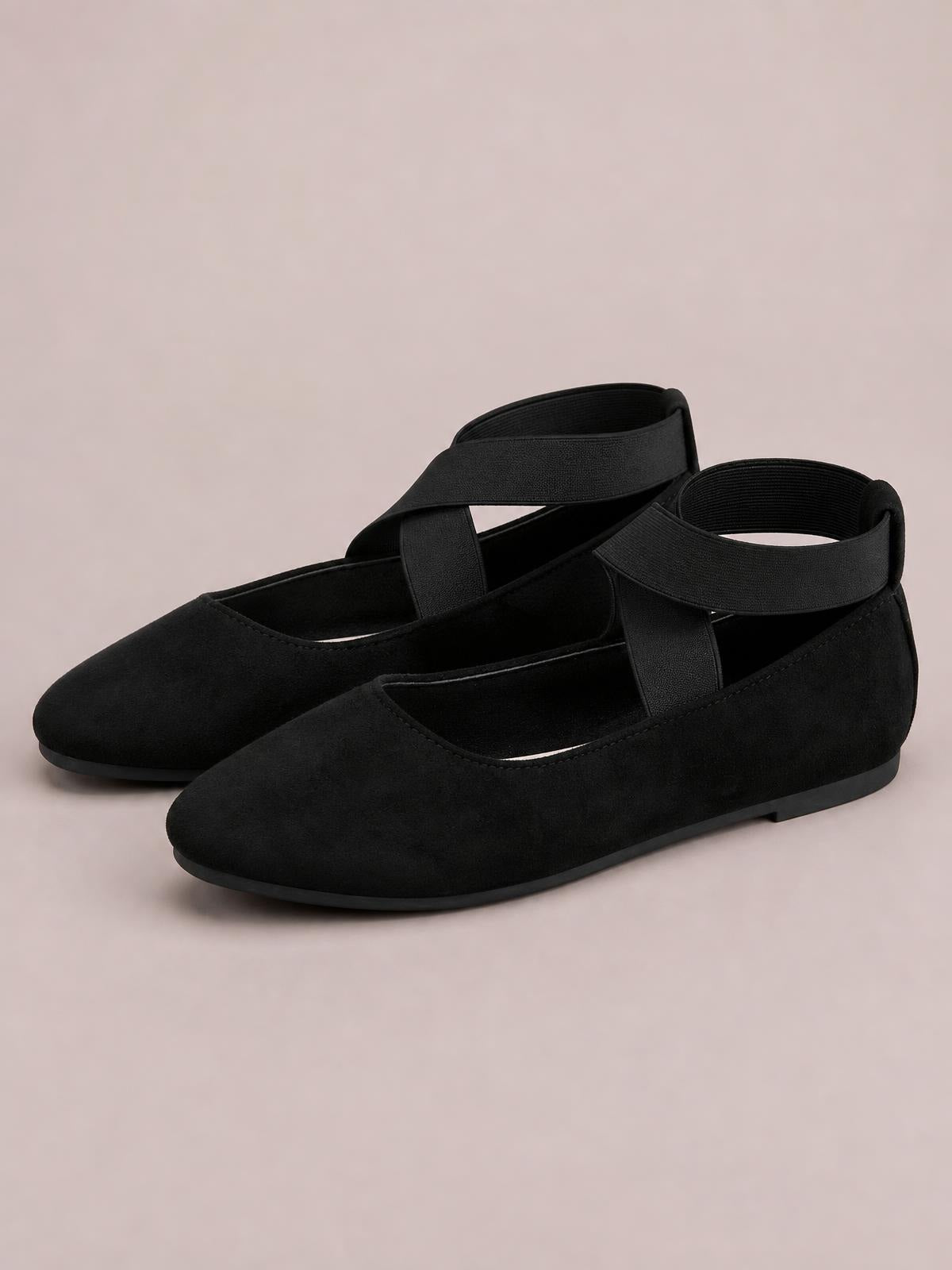 Black suede flat slip-ons feature a sleek pointed-toe silhouette, crisscross straps, and low rubber soles.