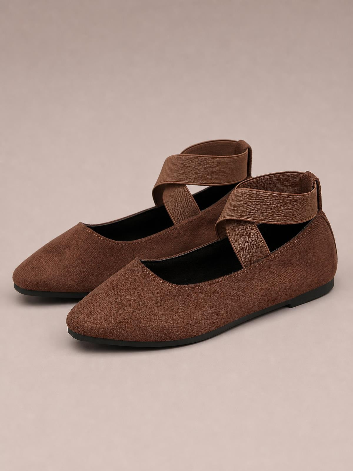 Brown suede-textured point-toe flat slip-ons feature crisscross straps, a low silhouette, and sturdy black rubber soles.