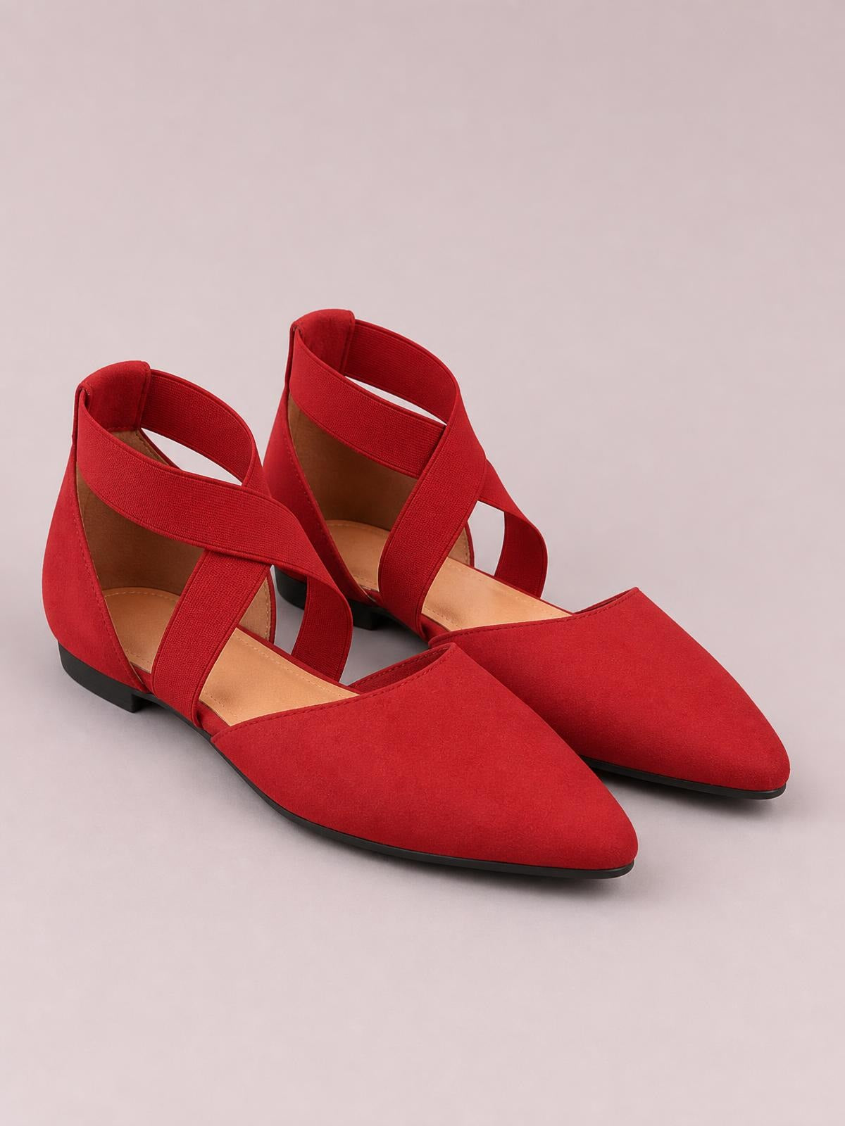 Red suede flat slip-ons feature pointed toes, crisscross straps, open sides, tan insoles, and low black rubber soles.