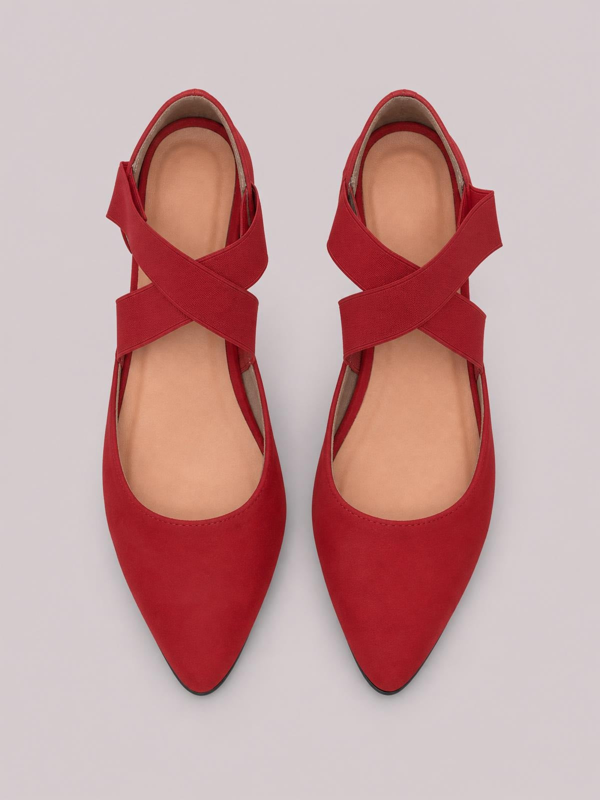 Pair of red suede flat slip-ons with pointed toes, crisscross straps, open sides, cushioned insoles, and slim rubber soles shown from above.