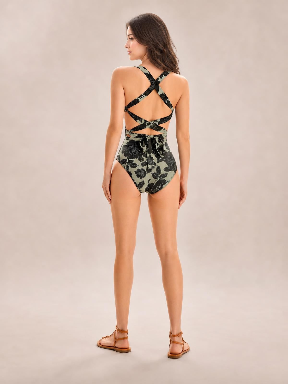 Model shown from behind in a floral-print one-piece swimsuit with crisscross back straps, tied waist details, and a fitted high-cut silhouette.
