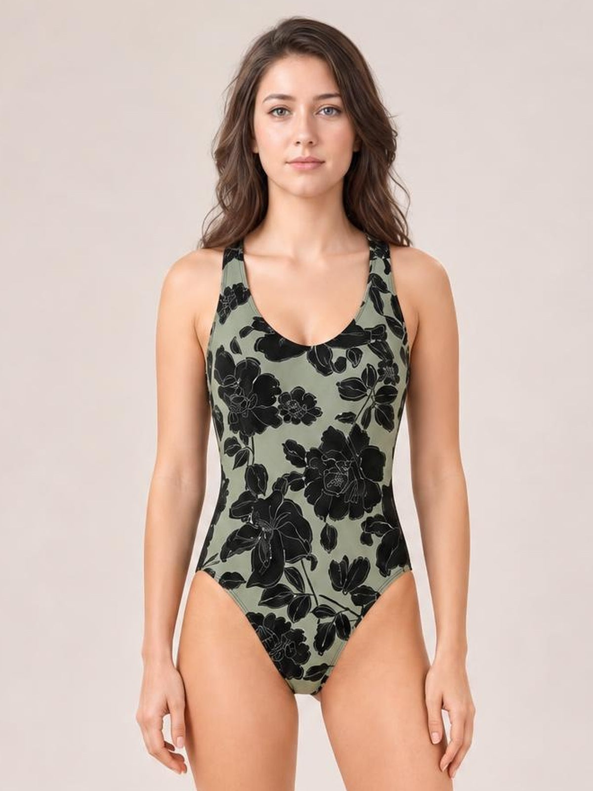 Front-facing model wears a fitted scoop neck one-piece swimwear style in muted sage green with bold black floral print and wide shoulder straps.