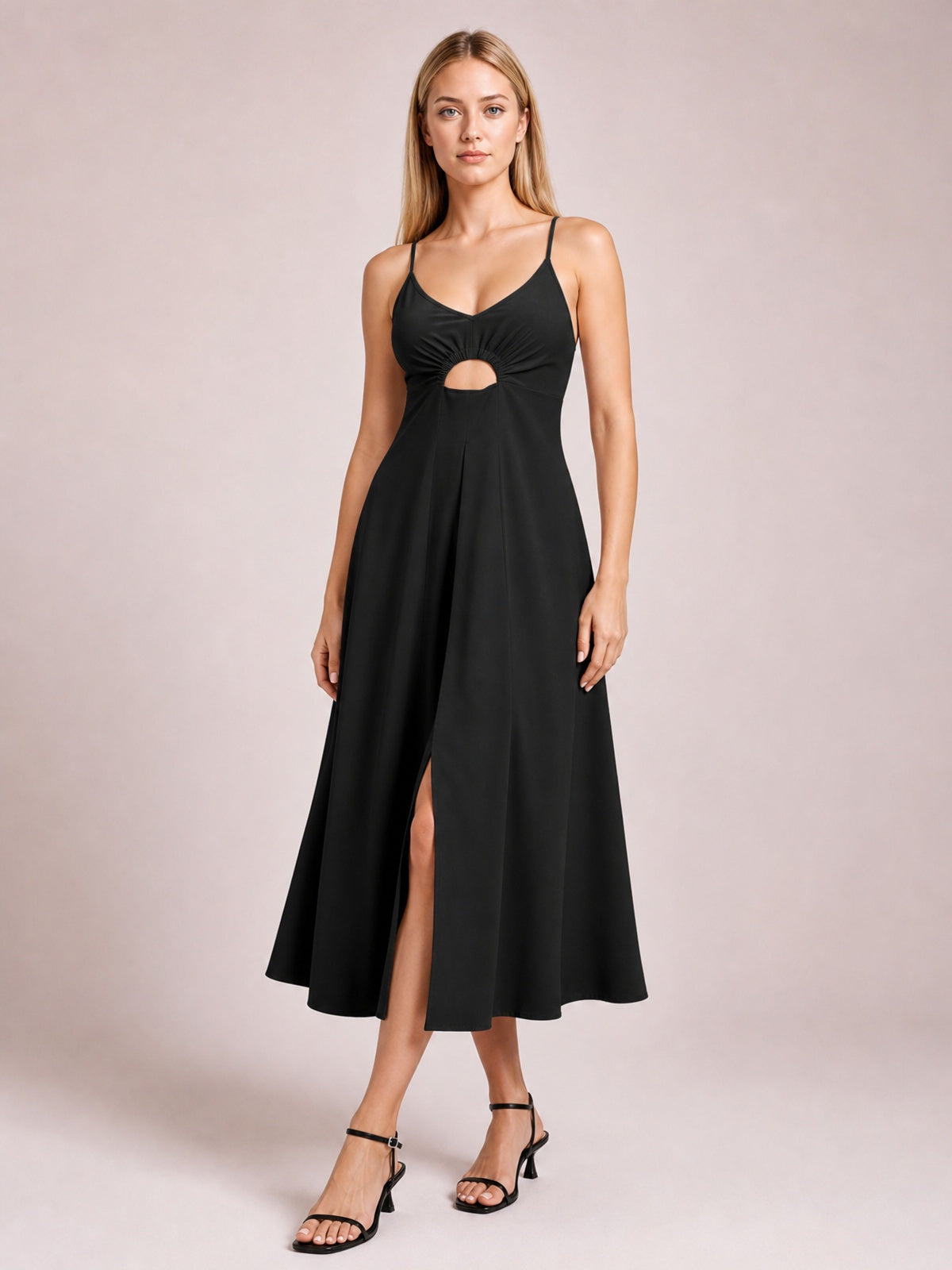 Model stands in a black spaghetti strap dress with a gathered bodice, front cutout, defined waist, and flowing midi-length A-line skirt.