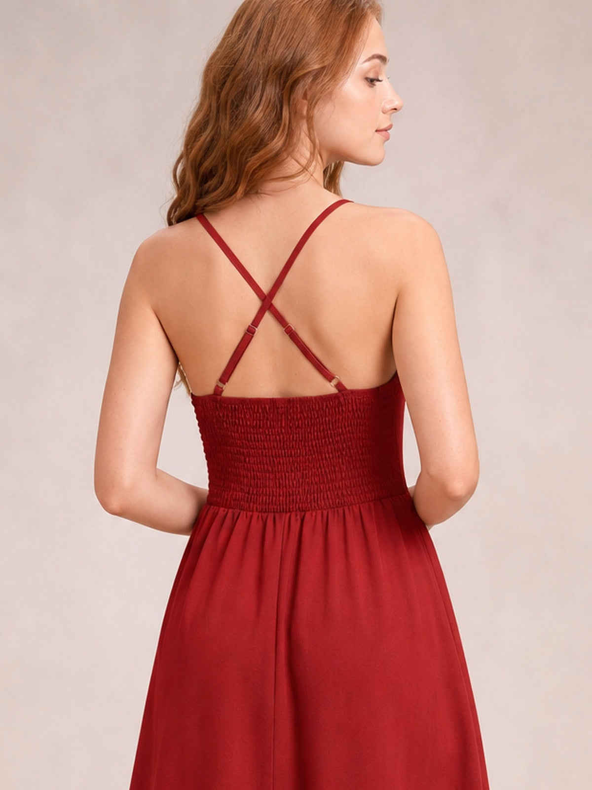 A model shows the back of a deep red crisscross smocked spaghetti strap dress with adjustable straps, a defined waist, and a flowing midi skirt.