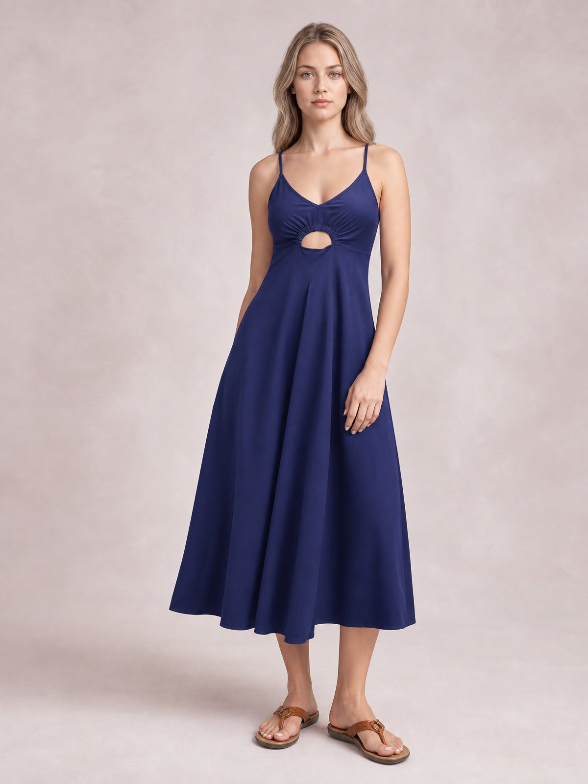 Model poses in a navy midi dress with spaghetti straps, a gathered bodice, front cutout, defined waist, and flowing A-line skirt.