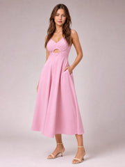 A model poses in a pink spaghetti-strap dress with a gathered bodice, front cutout, defined waist, side pockets, and a flowing midi-length skirt.