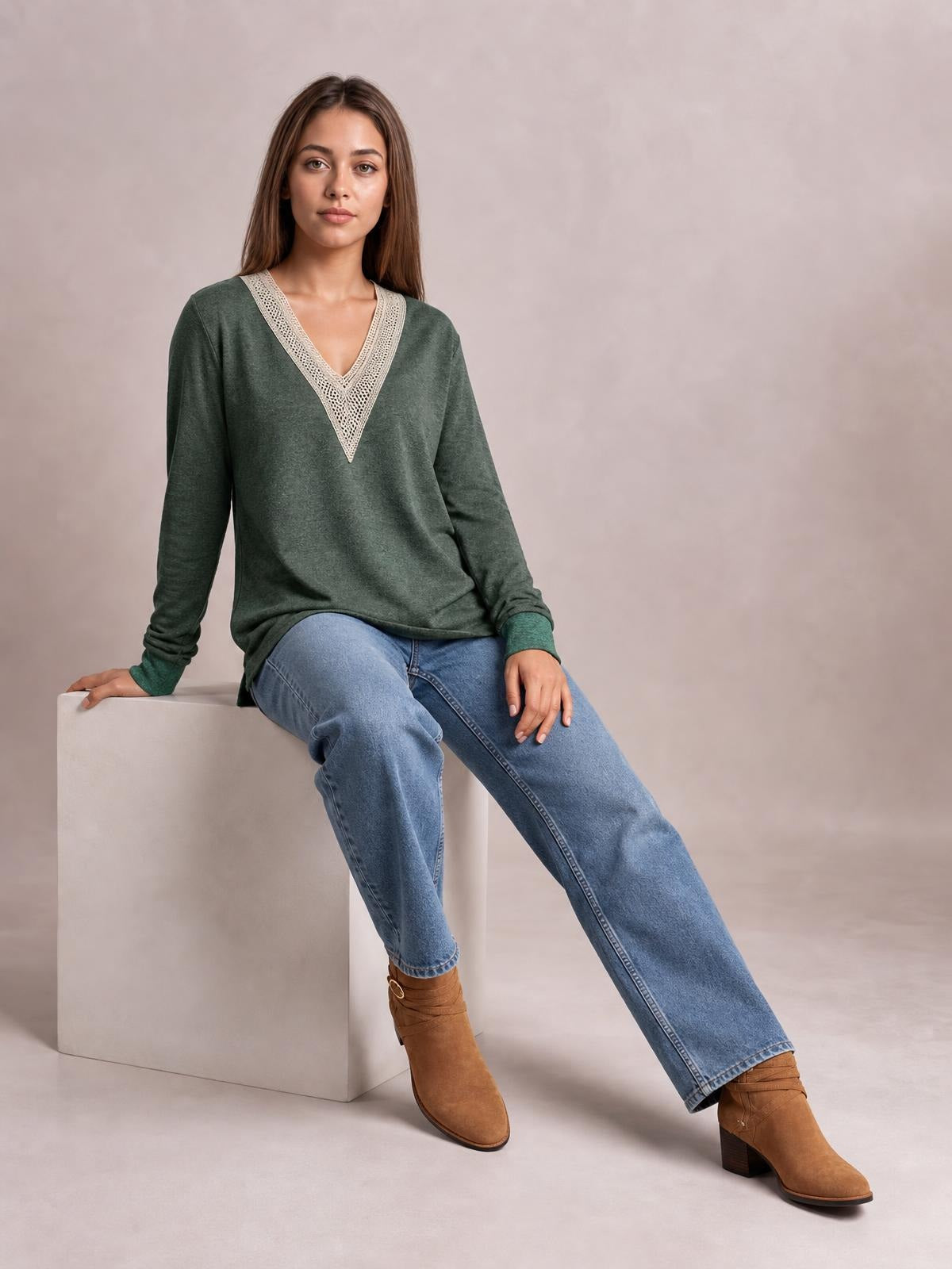 A seated model wears a forest green long-sleeve T-shirt with a contrasting crochet V-neck, relaxed silhouette, and side slit at the hem.