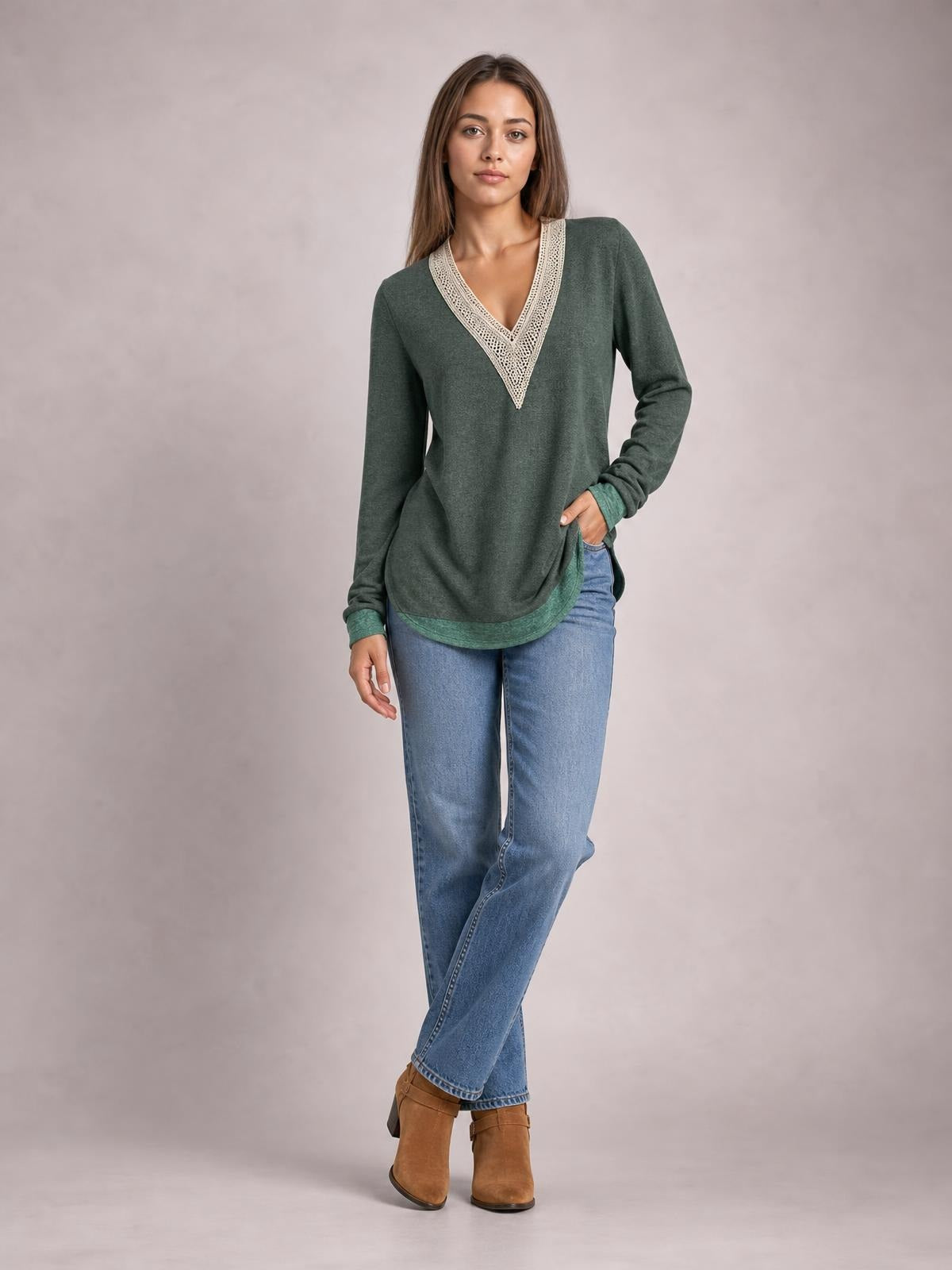 A model wears a forest green long-sleeve T-shirt with a contrasting crochet V-neck, relaxed silhouette, curved hem, and side slit, posing with one hand in her pocket.