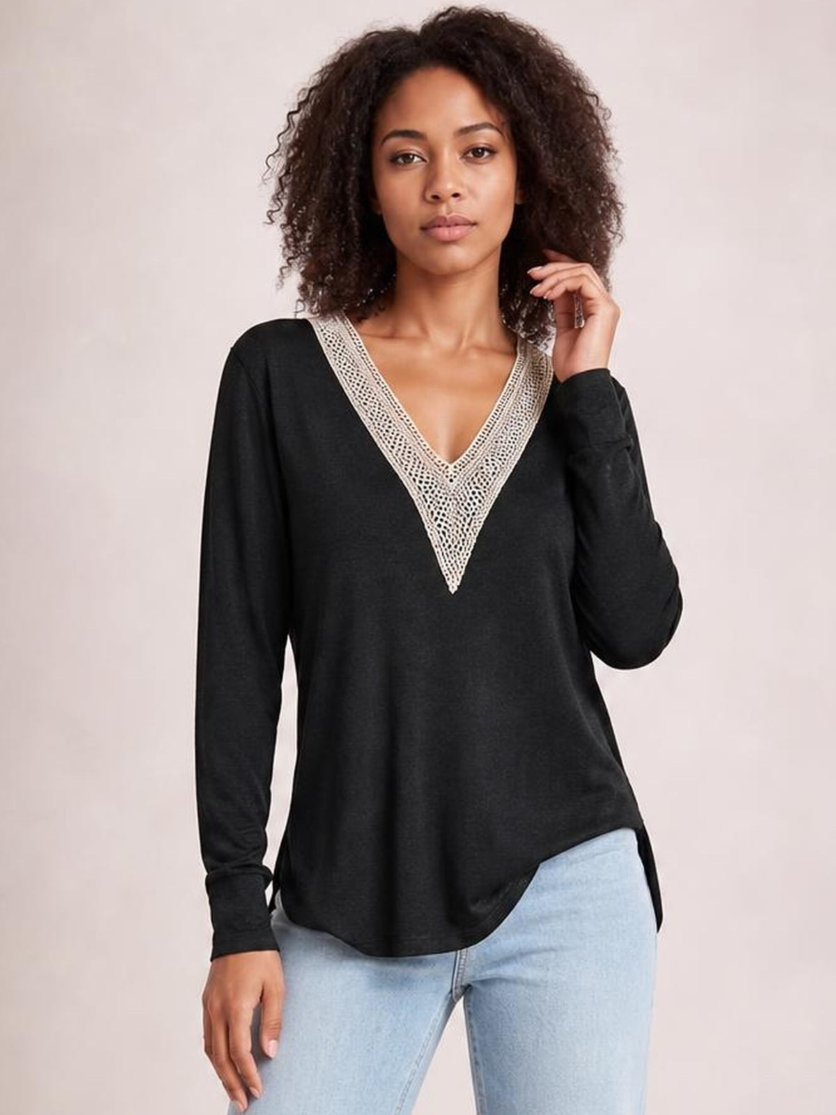 Model wears a black long-sleeve T-shirt with a contrasting crochet V-neck, relaxed silhouette, curved hem, and side slit details.