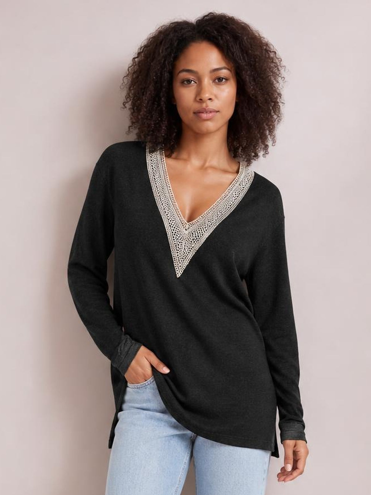 Model poses in a black long-sleeve T-shirt with a contrasting crochet V-neck, relaxed silhouette, and side slits over light jeans.