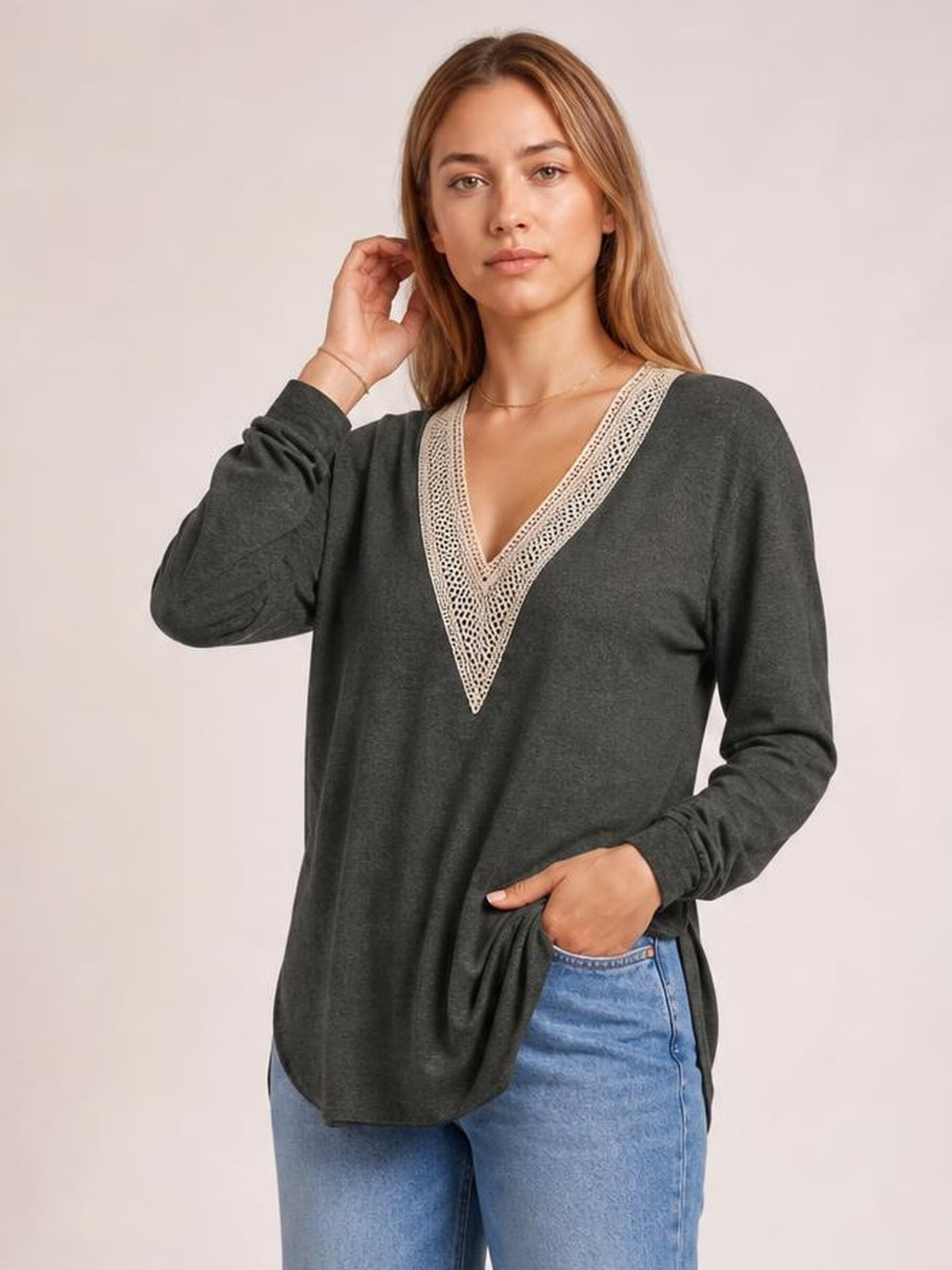 A model poses in a charcoal long-sleeve T-shirt with a contrasting crochet V-neck trim, relaxed silhouette, and visible side slit at the hem.