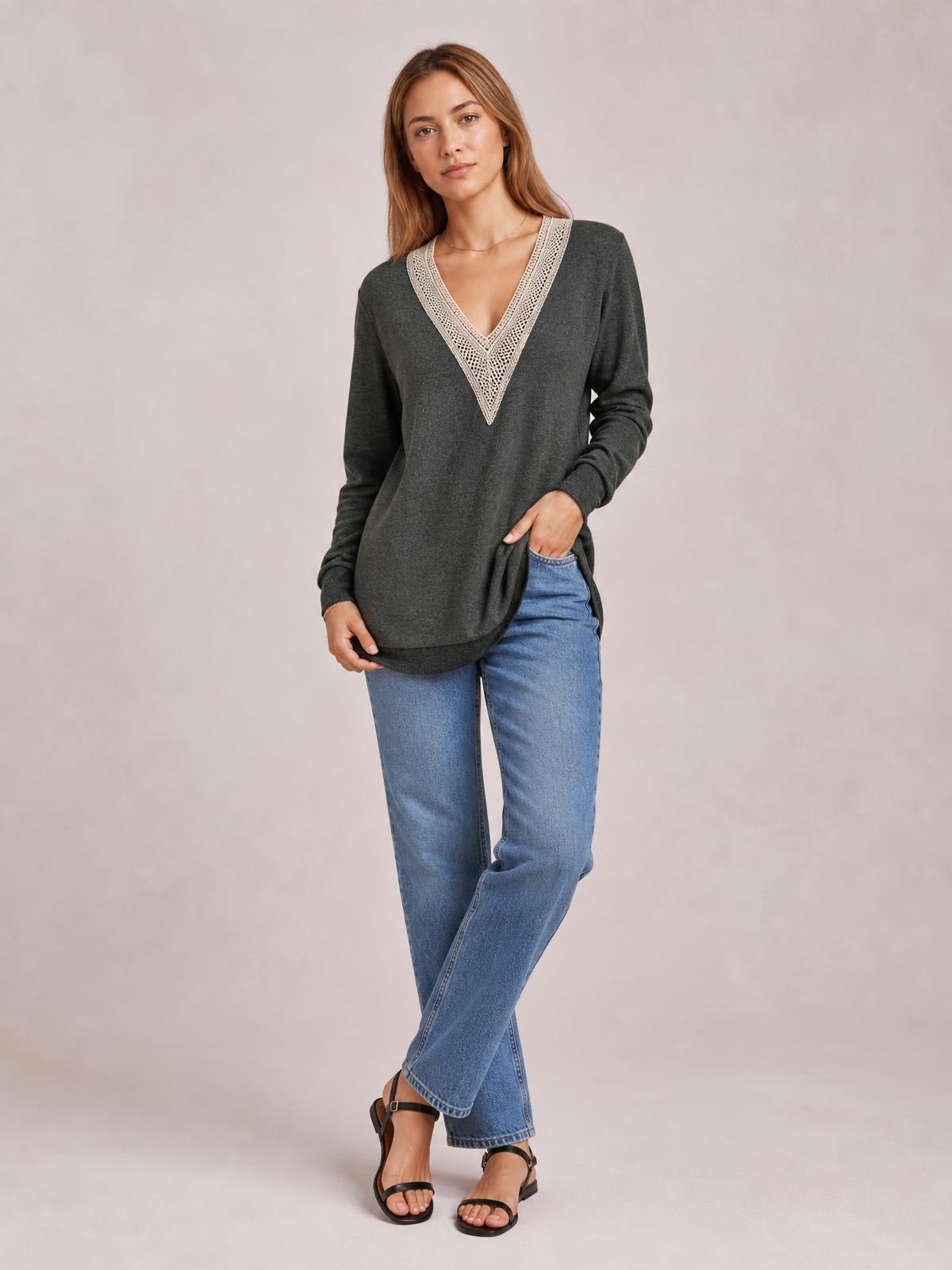 A woman poses in a charcoal long-sleeve T-shirt with a cream crochet-trimmed V-neck, relaxed silhouette, curved hem, and visible side slit.