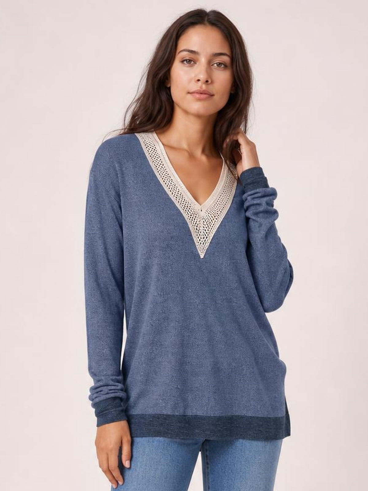Model wears a loose blue long-sleeve T-shirt with a contrasting crochet V-neck trim and darker hem, posing with one hand touching her hair.