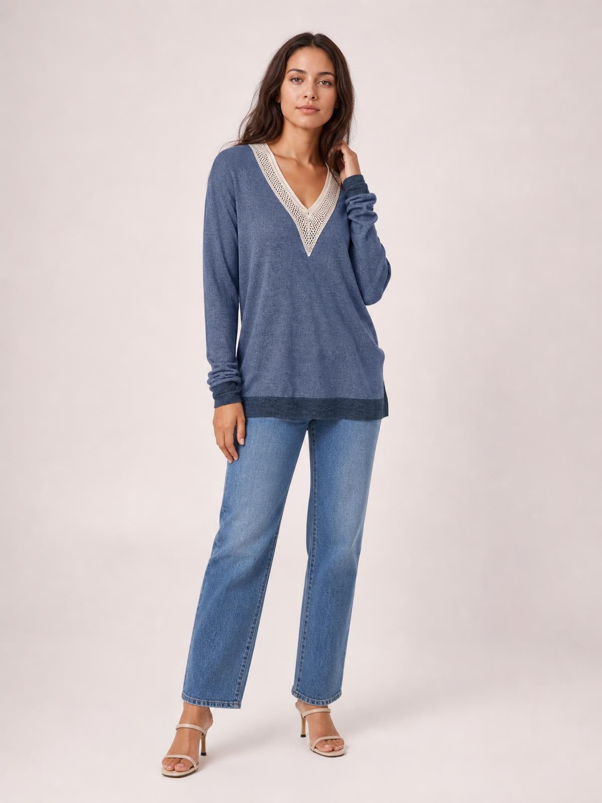 Model wears a blue long-sleeve T-shirt with a contrasting crochet V-neck, relaxed silhouette, and darker hem panel, standing with one hand near her hair.