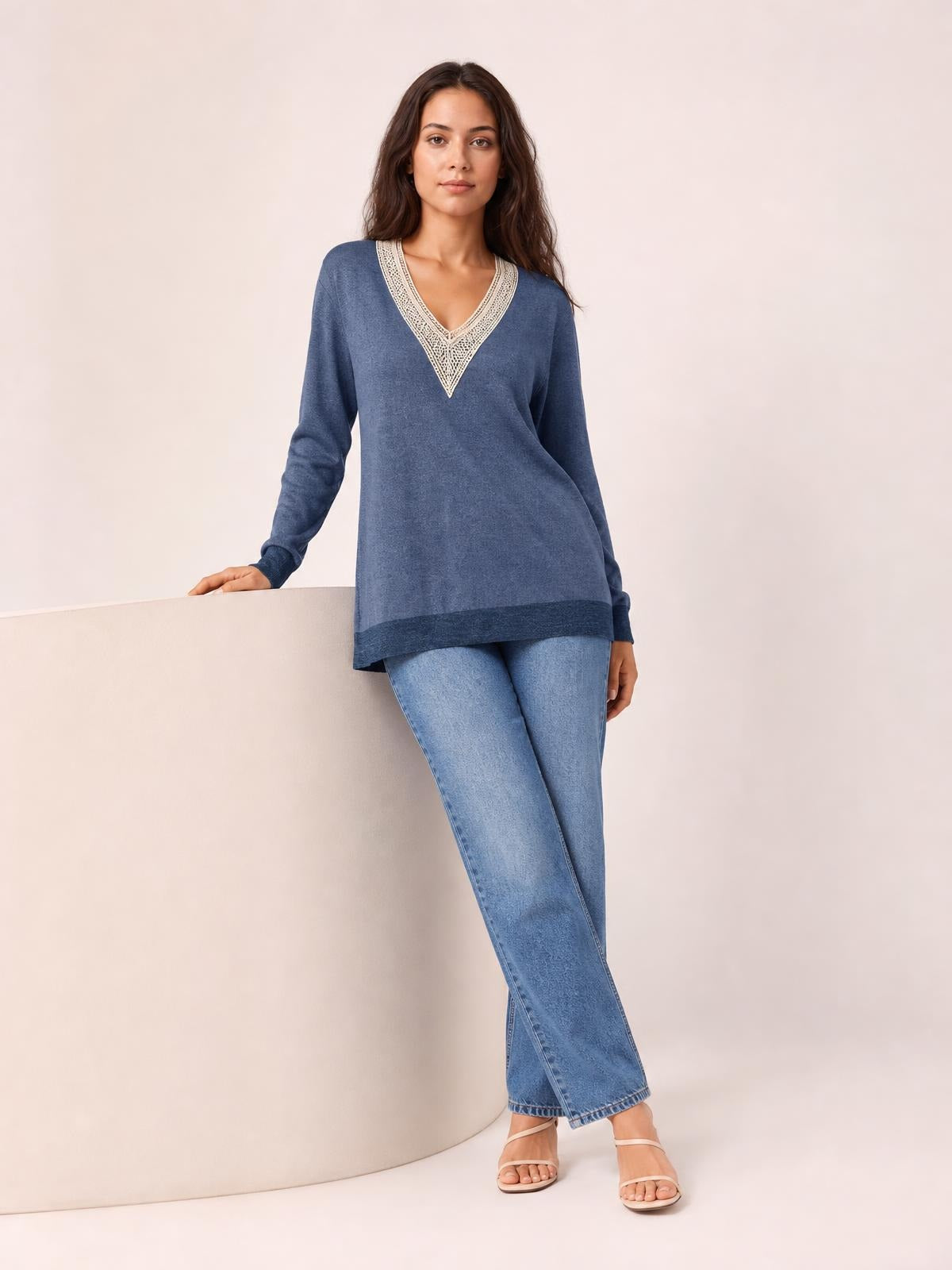 Model wears a blue crochet contrast V-neck long sleeve T-shirt with a relaxed, slightly flared silhouette, leaning casually with one hand resting nearby.
