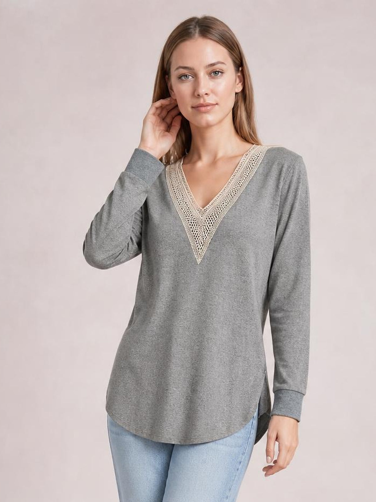 Model poses with one hand near her neck wearing a gray long-sleeve T-shirt with a contrasting crochet V-neck, relaxed silhouette, and side slits.