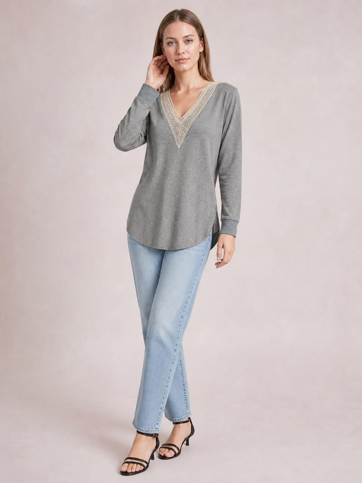 Model poses in a gray long-sleeve T-shirt with a contrasting crochet-trimmed V-neck, relaxed tunic silhouette, curved hem, and side slit.