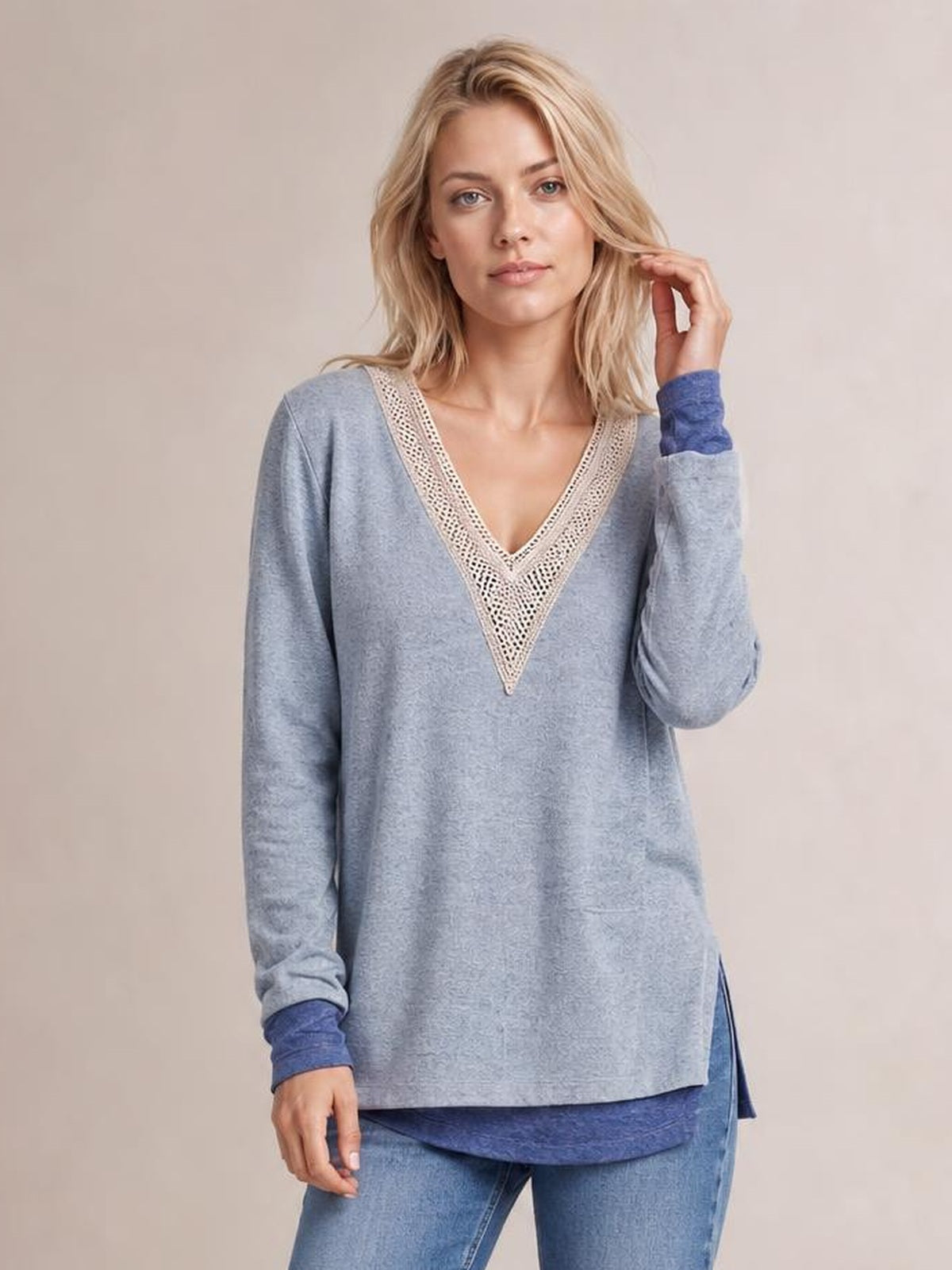A model wears a blue-gray crochet contrast V-neck long-sleeve T-shirt with a relaxed silhouette and side slit, touching her hair in a casual pose.