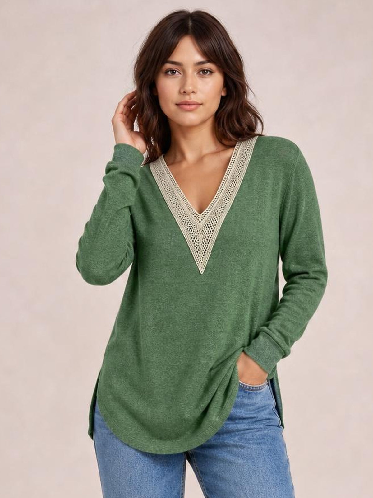 A model poses in a relaxed green long-sleeve T-shirt with a contrasting crochet-trimmed V-neck, side slits, and a loose curved-hem silhouette.