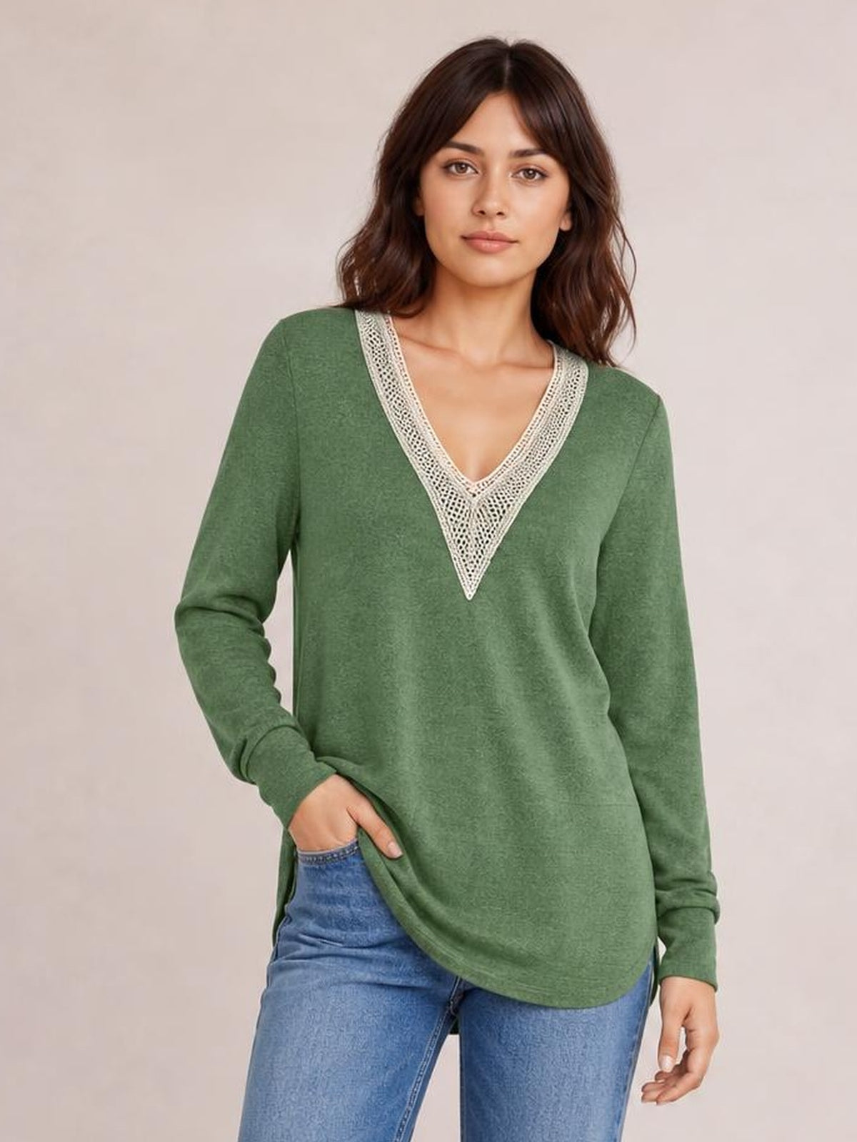 A woman models a relaxed green long-sleeve T-shirt with a contrasting crochet V-neck, curved hem, and side slit, posing with one hand in her pocket.