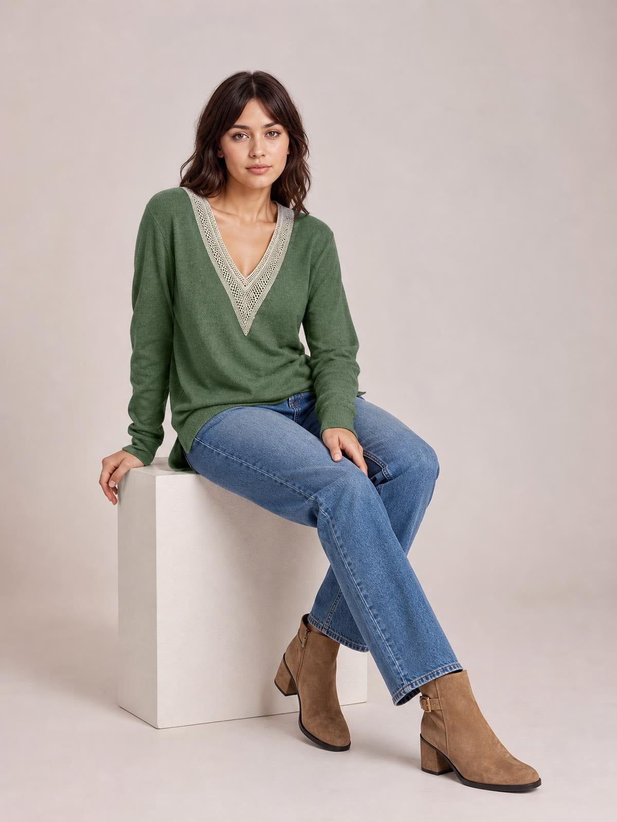 A model sits with crossed legs wearing a green long-sleeve T-shirt with a crochet contrast V-neck, relaxed silhouette, ribbed cuffs, and side slits.
