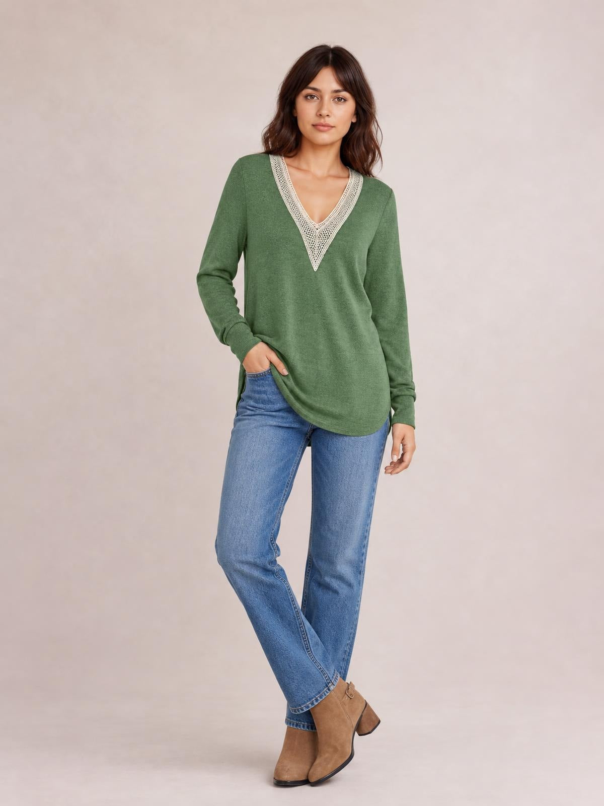 Model wearing a green long-sleeve T-shirt with a contrasting white crochet V-neck, relaxed silhouette, and curved slit hem, posed with crossed legs.