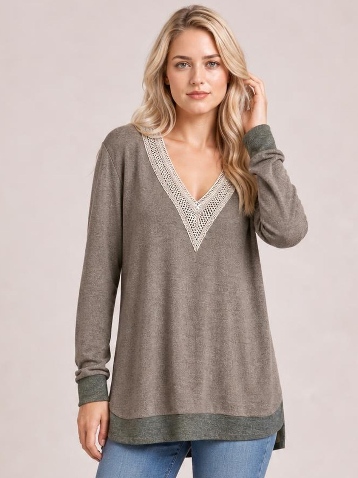 A model poses in a taupe crochet contrast V-neck long sleeve T-shirt with a relaxed tunic silhouette, curved hem, and visible side slit.