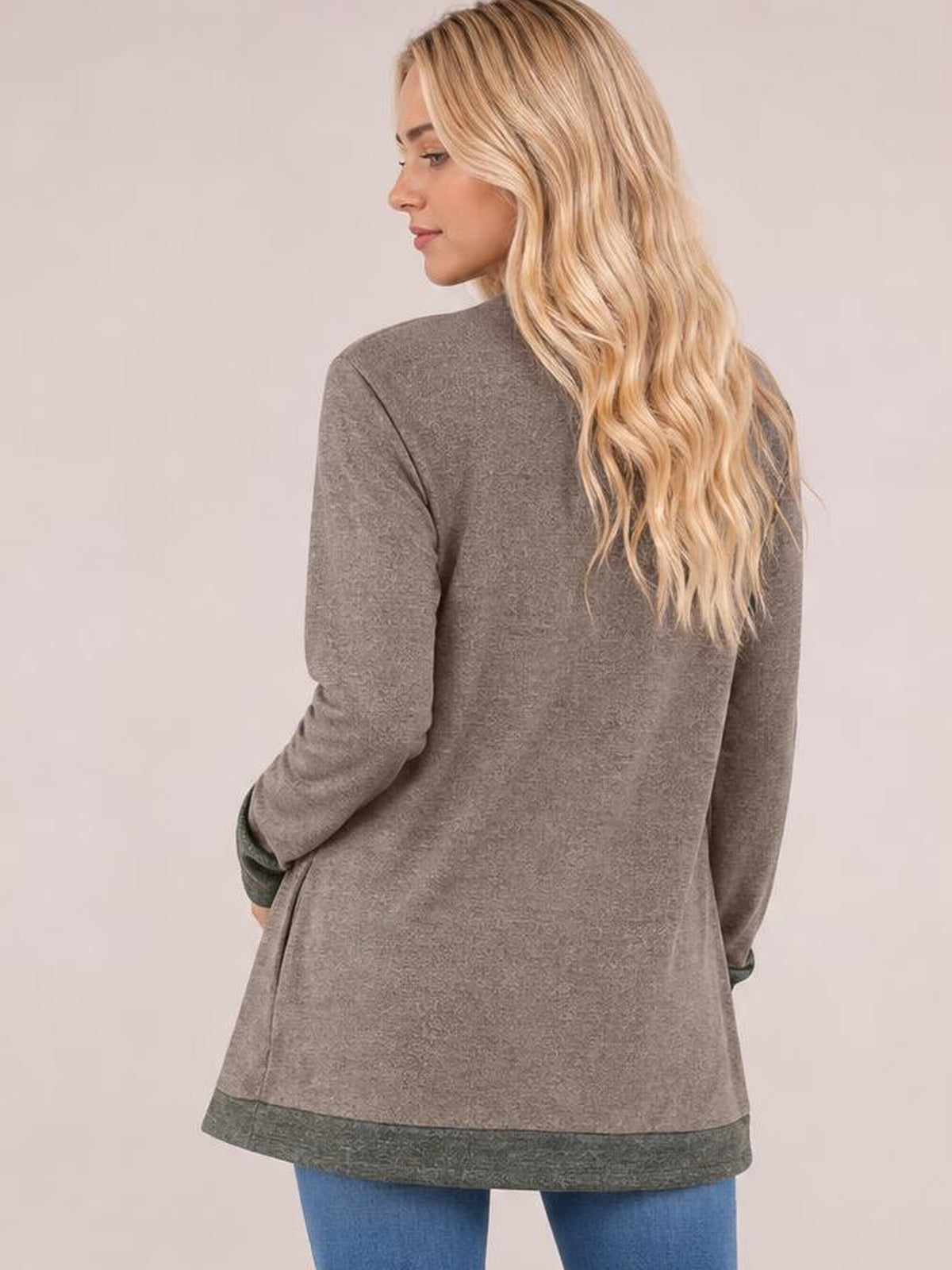 A model poses turned away in a taupe long-sleeve T-shirt with contrast dark cuffs and hem, relaxed long silhouette, and side slit.