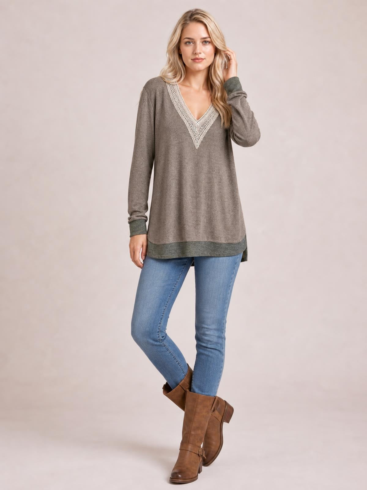A model poses with crossed legs in a taupe long-sleeve T-shirt featuring a contrast crochet V-neck, relaxed tunic silhouette, and side slit.