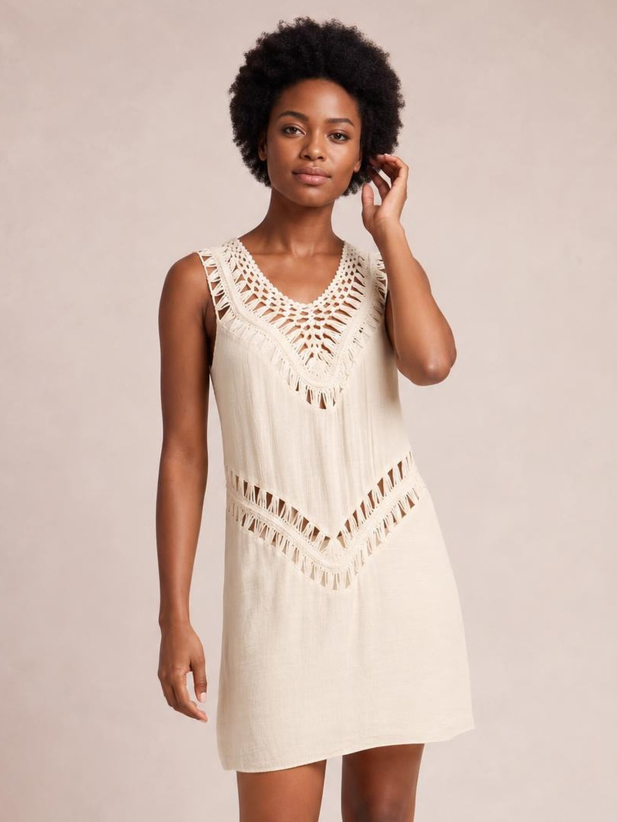 Model poses in a cream beach cover up dress with a relaxed straight silhouette, crochet V-neck detail, cutout accents, and fringe trim.