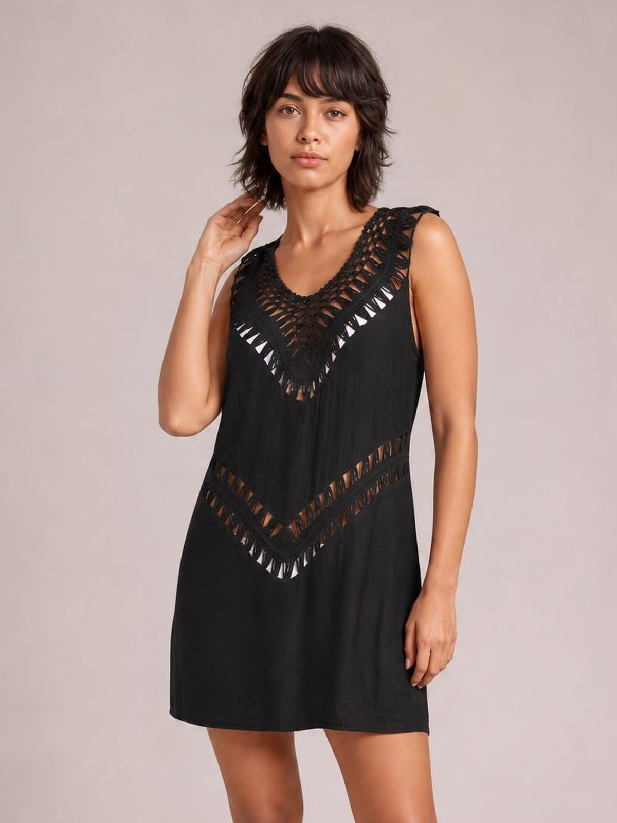 Model poses in a black beach cover up dress with a relaxed straight silhouette, sleeveless cut, and crochet-style cutout trim around the neckline and waist.