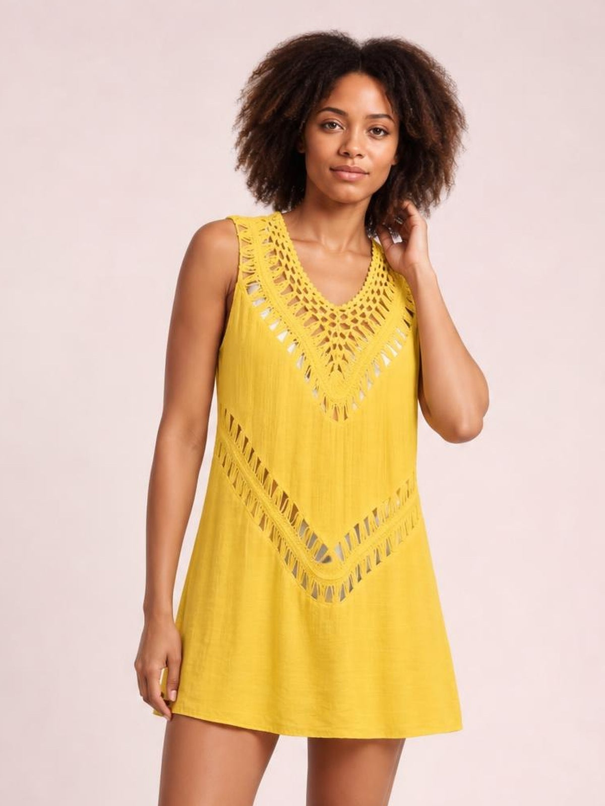 Model wears a yellow beach cover up dress with sleeveless styling, crochet cutout detailing, and a relaxed A-line silhouette while touching her hair.