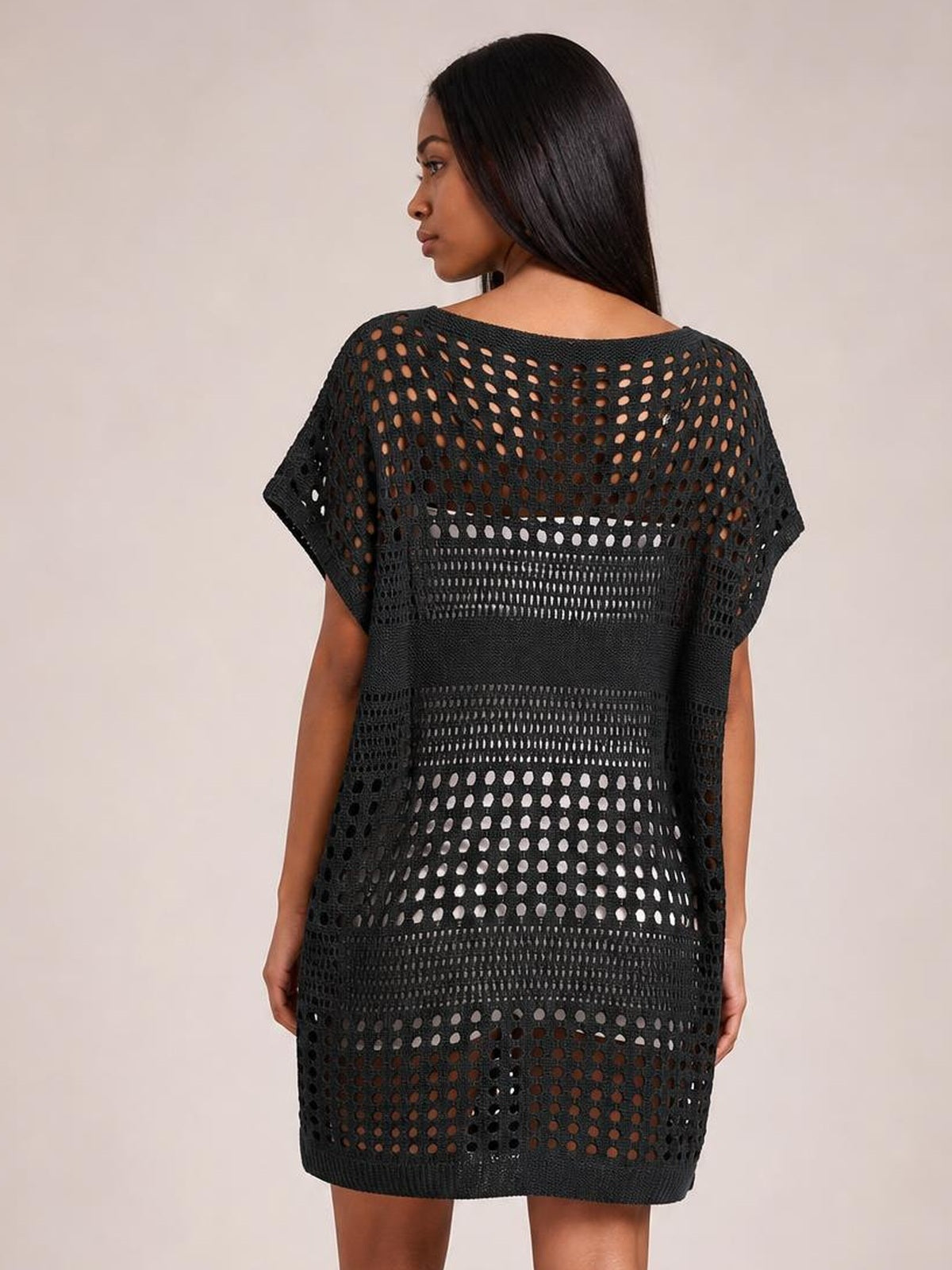 A model wears a black crochet knit beach cover-up dress from the back, featuring a loose oversized silhouette, short sleeves, and openwork cutout panels.