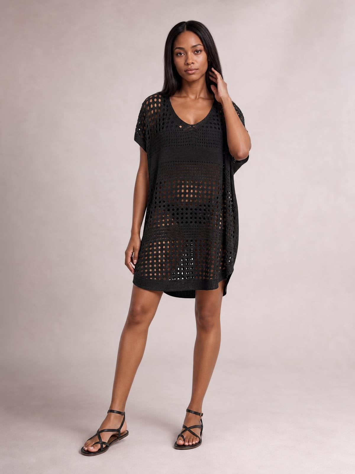Model poses in a black crochet knit beach cover up dress with a loose straight silhouette, short sleeves, scoop neckline, and open cutout construction.