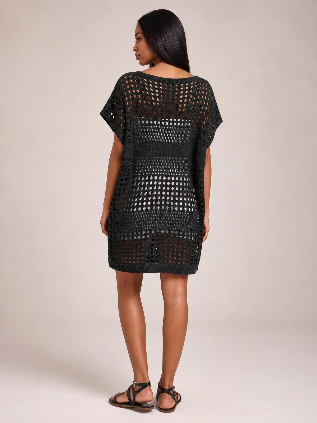 Model shown from the back wearing a black crochet knit beach cover up dress with an openwork cutout pattern, short sleeves, and a straight knee-length silhouette.