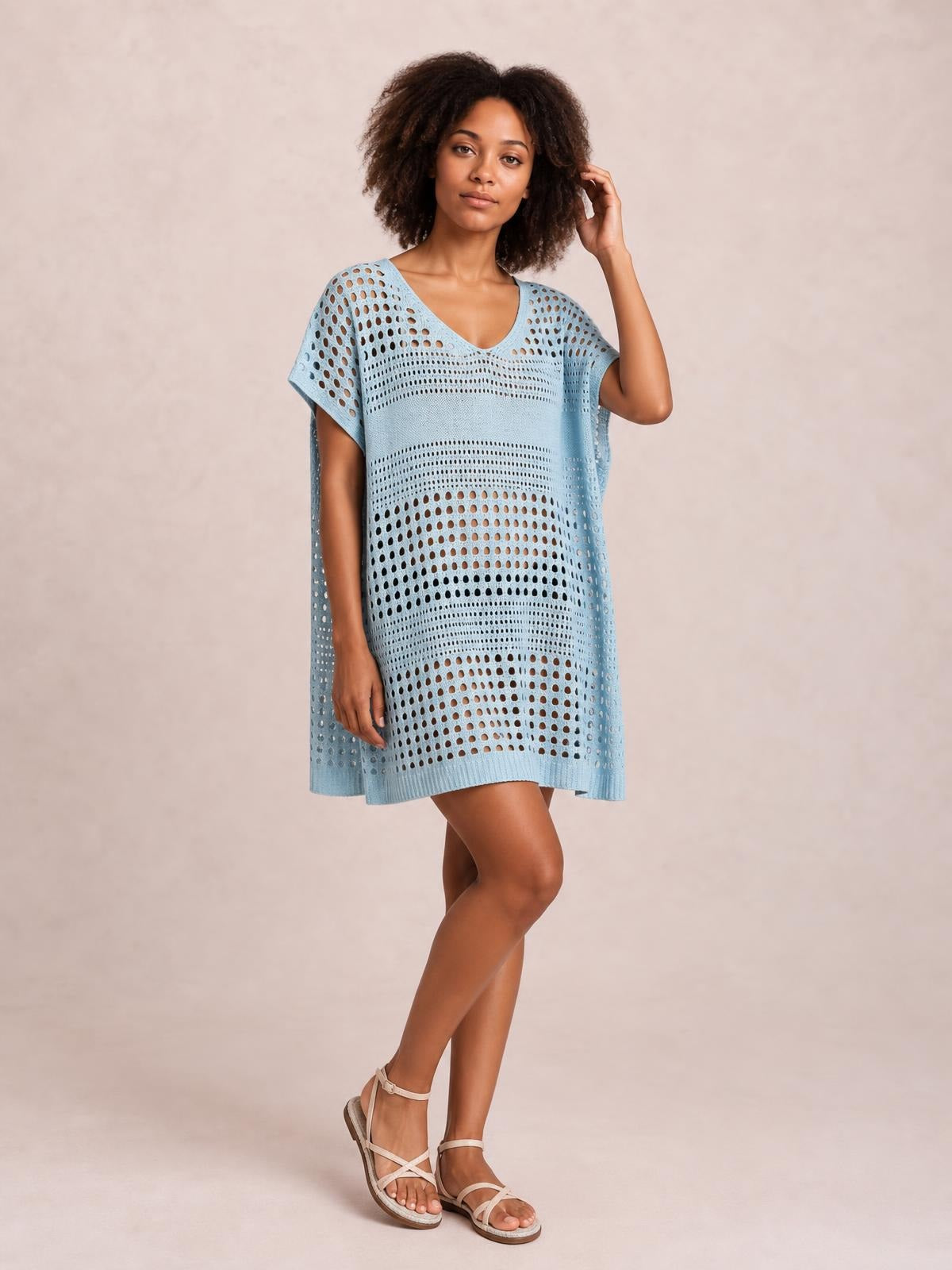 Model wearing a light blue crochet knit beach cover up dress with a V-neck, cutout pattern, short sleeves, and a relaxed tunic silhouette.