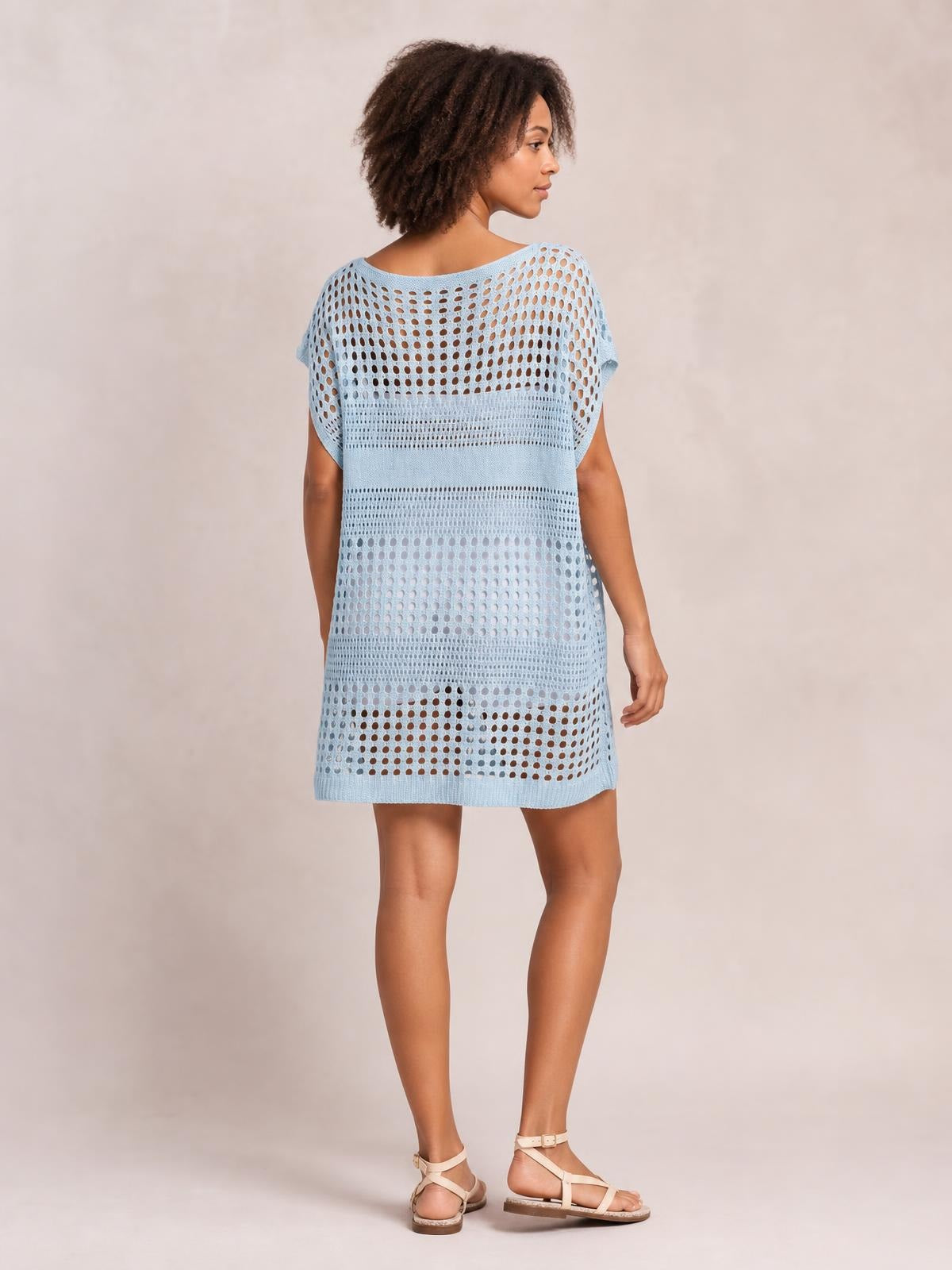 Model looks over her shoulder in a pale blue crochet knit beach cover-up dress with short sleeves, openwork cutout construction, and a relaxed knee-length silhouette.