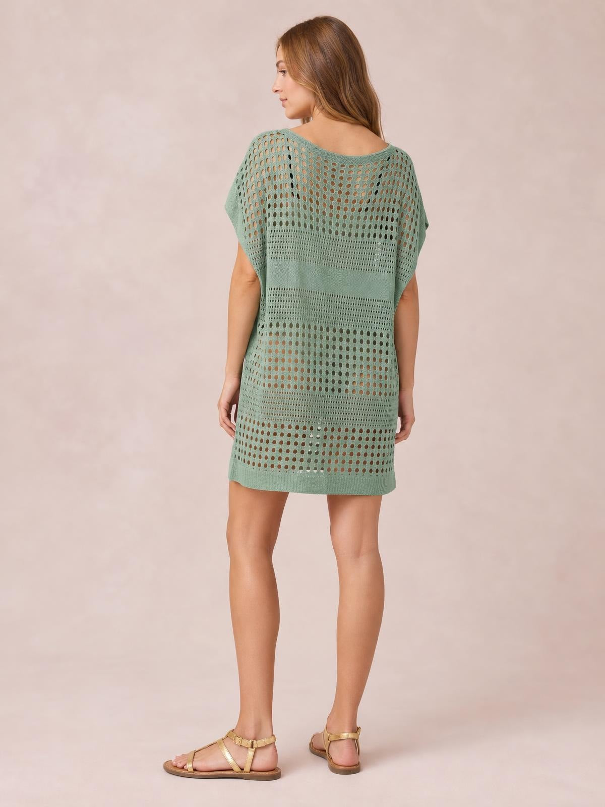 Model shown from the back in a sage green crochet knit beach cover up dress with short sleeves, openwork cutouts, a relaxed straight silhouette, and above-knee hem.