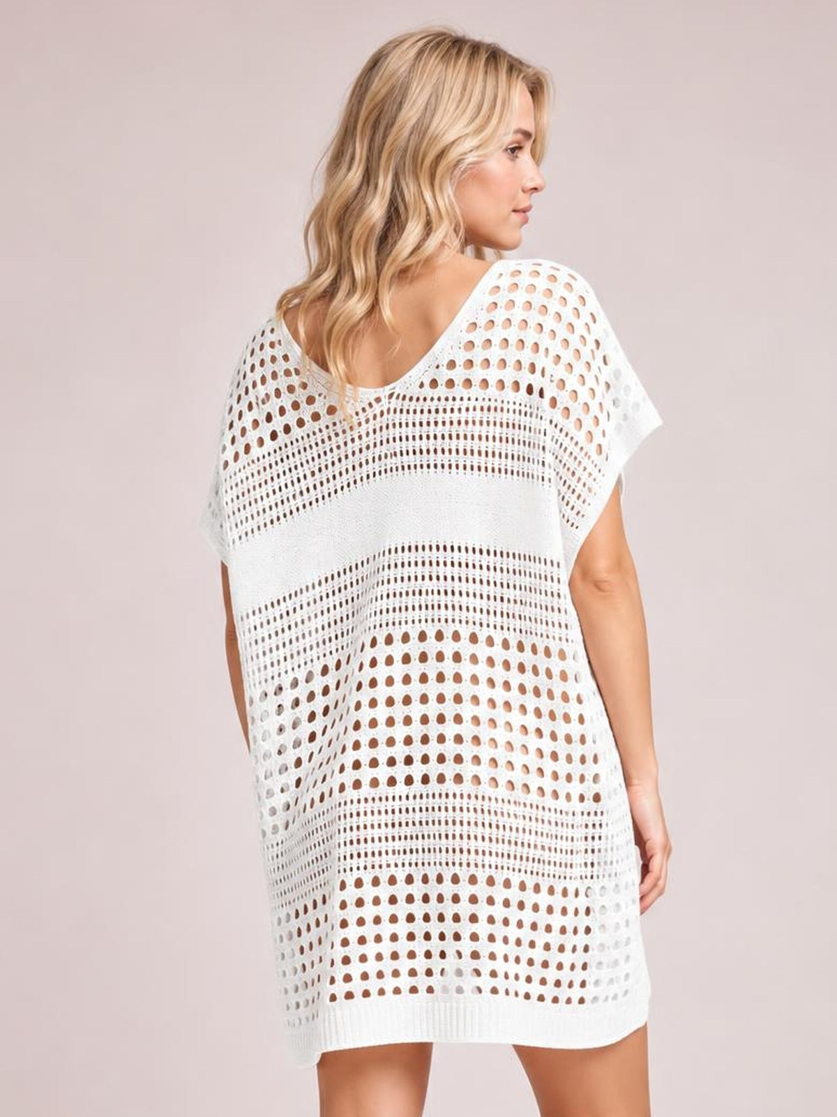 Model wearing a white crochet knit beach cover up dress with a relaxed, loose silhouette, short sleeves, openwork cutout pattern, and ribbed hem.
